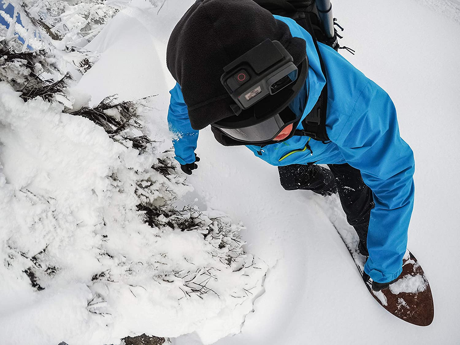 Un snowboarder con chaqueta azul trepa en la nieve, cámara en casco.