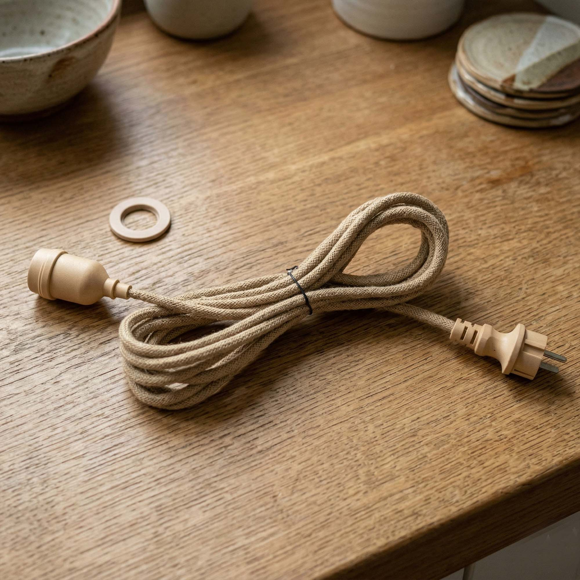 Ein beige Stoffkabel mit Stecker und Fassung liegt auf einem Holztisch.
