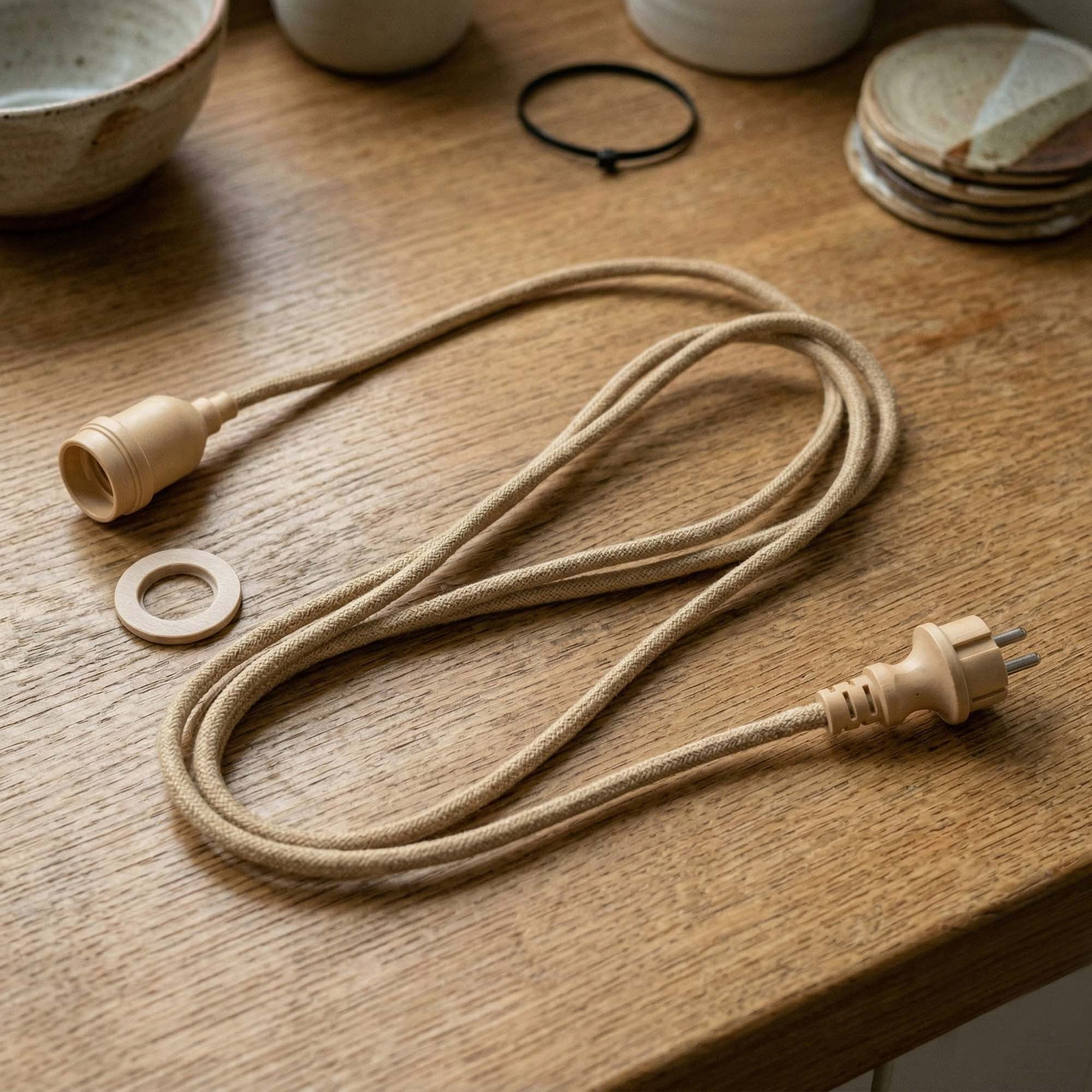 Ein beiges Stoffkabel mit Stecker und Fassung liegt auf einem Holztisch.