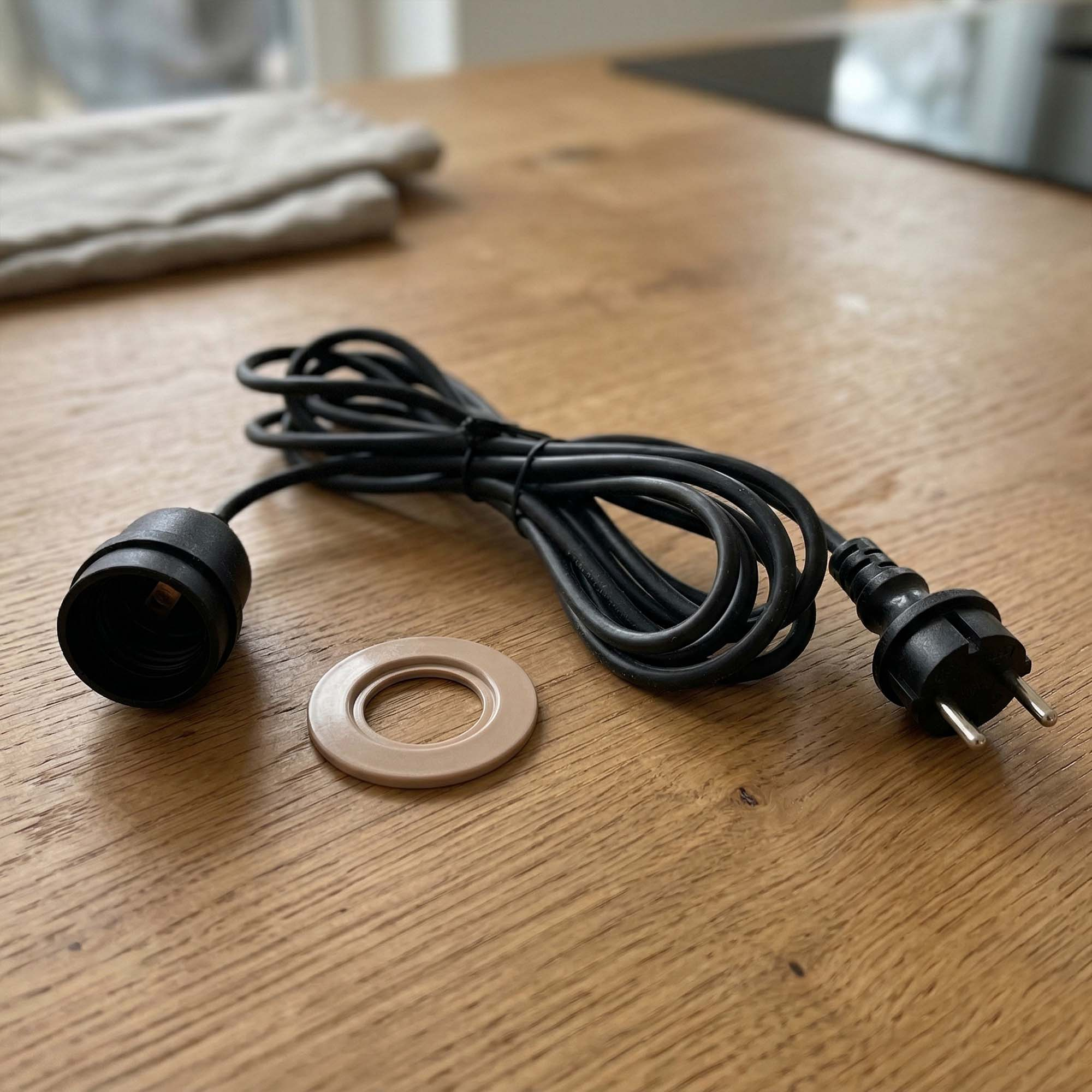Schwarzes Kabel mit Stecker, Lampenfassung und Ring auf Holztisch.