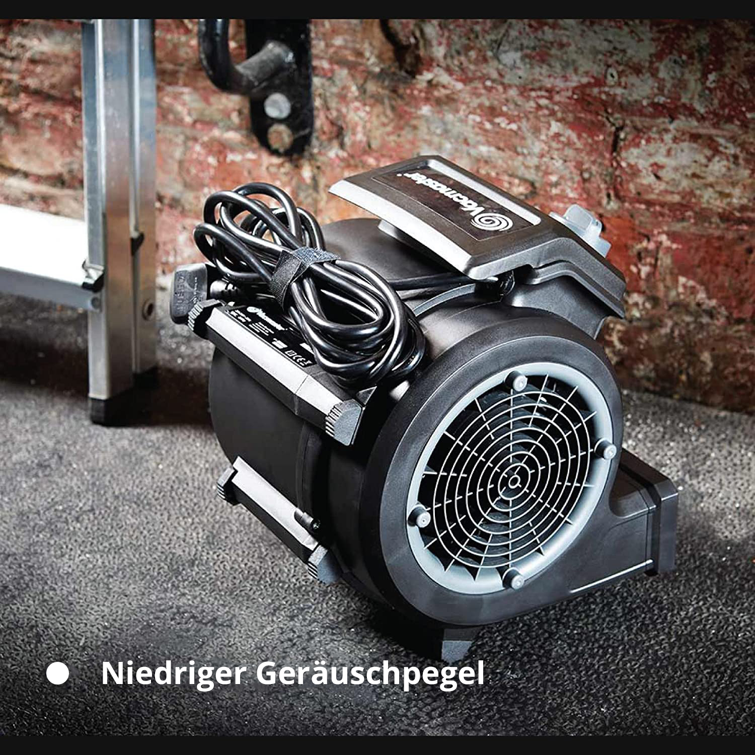Ein schwarzer Gebläsemotor mit Kabel, Leiter und Ziegelwand im Hintergrund.