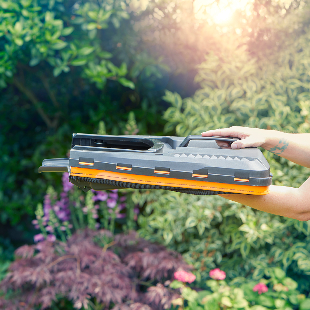Grauer Fensterreiniger mit orangefarbenem Akzent wird im Garten gehalten.