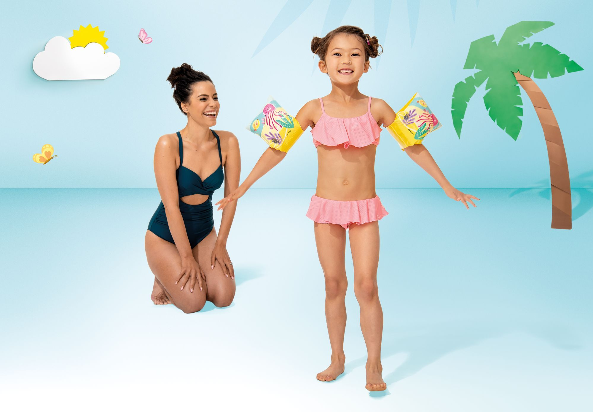 Kobieta w granatowym stroju kąpielowym i dziewczynka w różowym bikini z rękawkami.