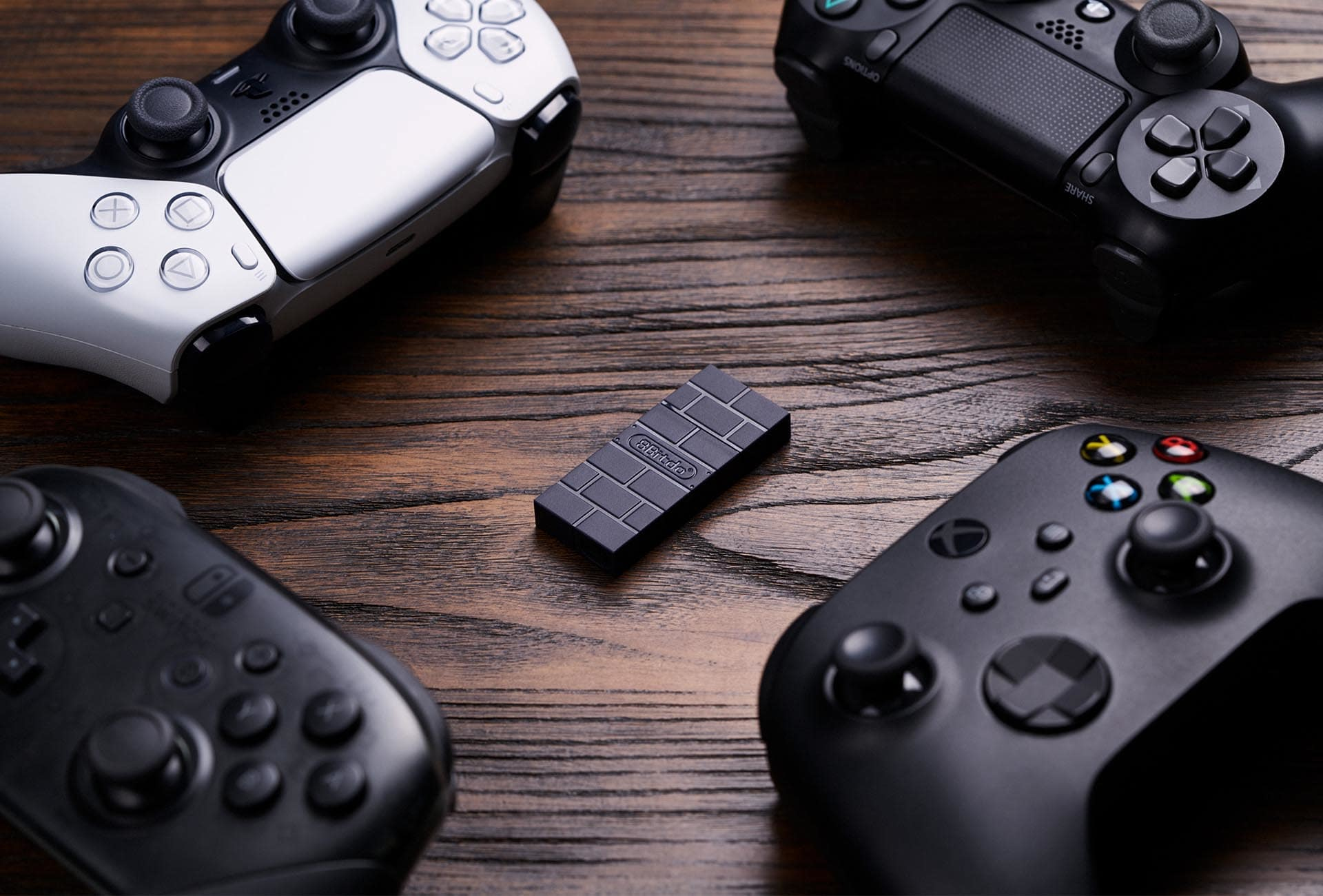 Quattro controller di gioco e un adattatore nero a motivi di mattoni su tavolo di legno.