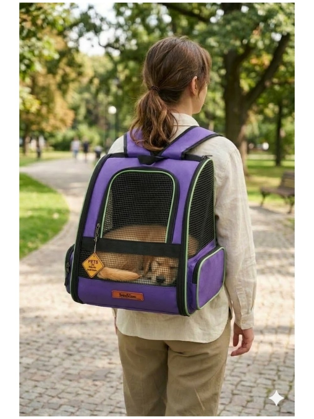 Bir kişi parkta içinde köpek olan mor bir sırt çantası taşıyor.