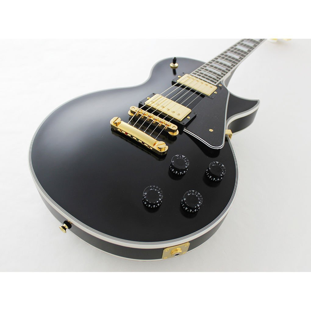 Beyaz arka plan üzerinde altın donanım ve düğmelere sahip siyah elektro gitar.