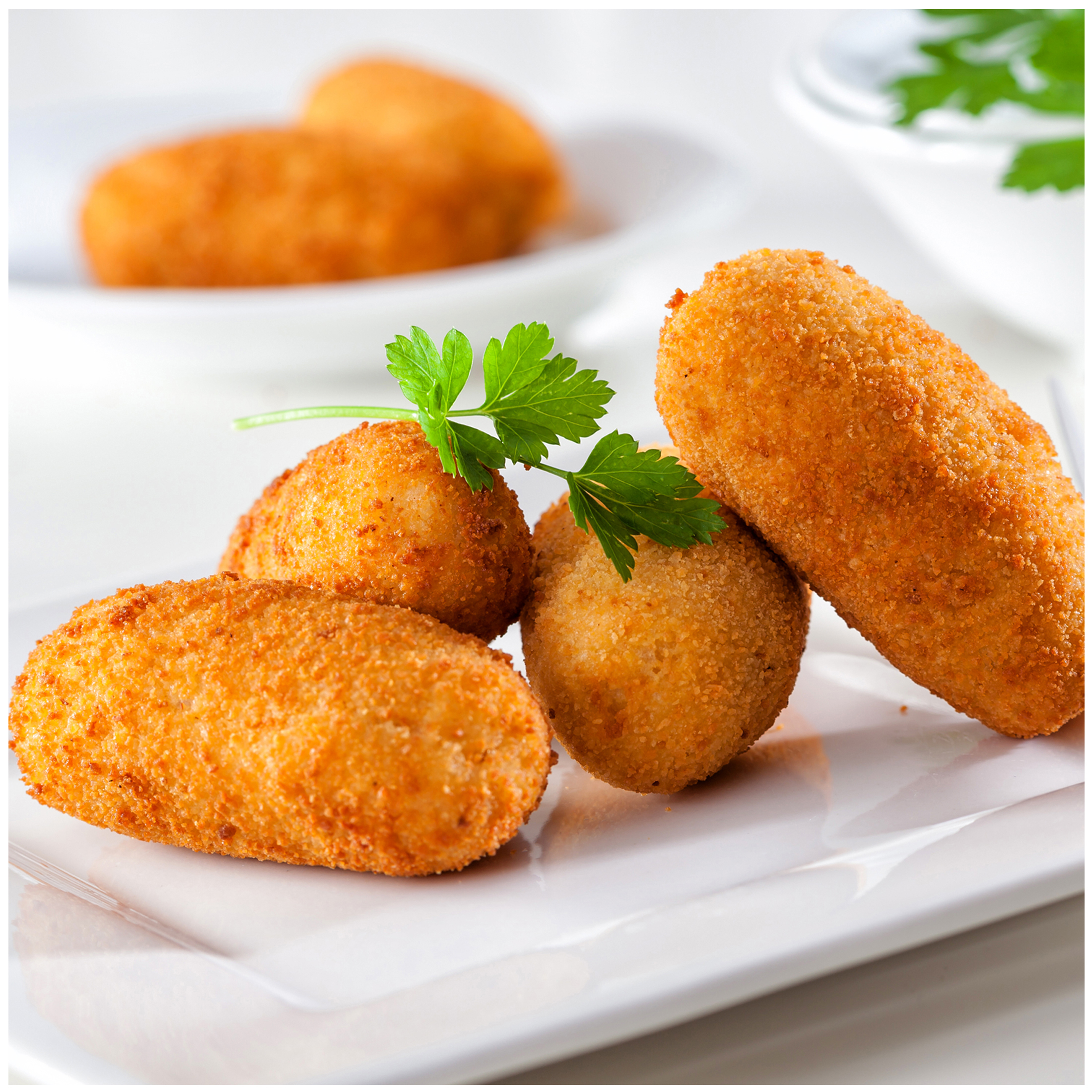 Vier goudbruine kroketten op een wit bord, gegarneerd met peterselie.