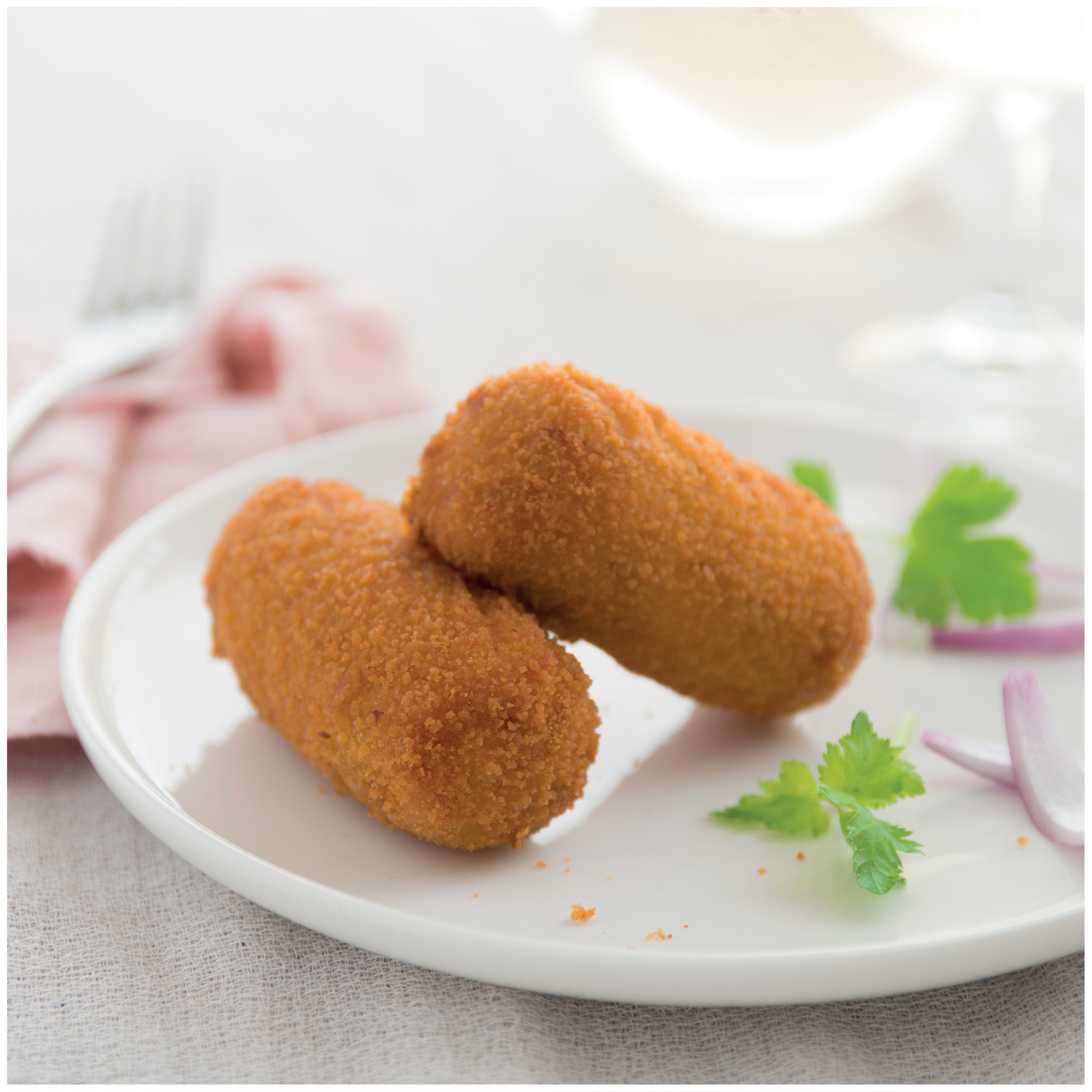 Due crocchette dorate su piatto bianco con prezzemolo e cipolla rossa.