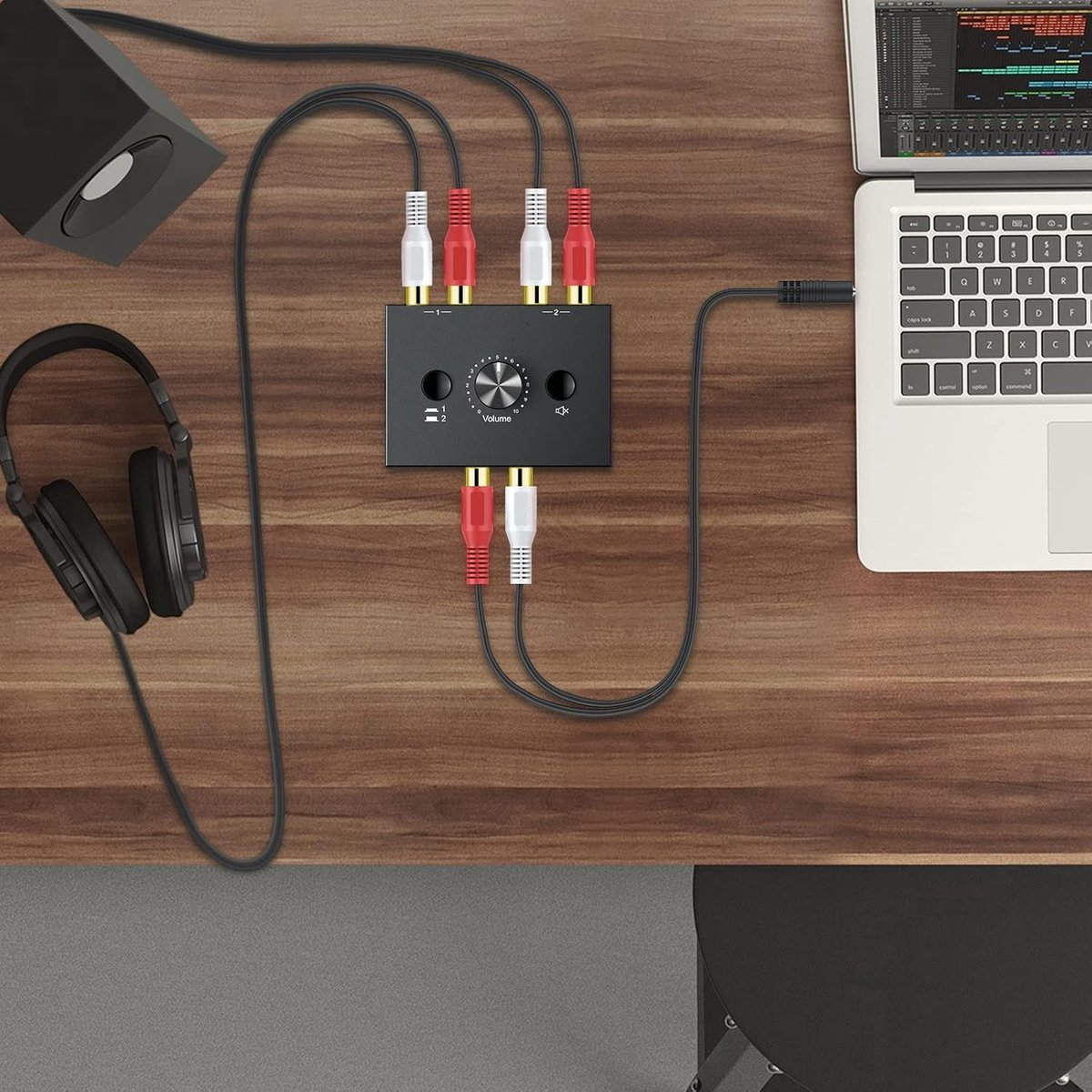 Een audio-splitter met kabels, koptelefoon, luidspreker en laptop op een houten bureau.