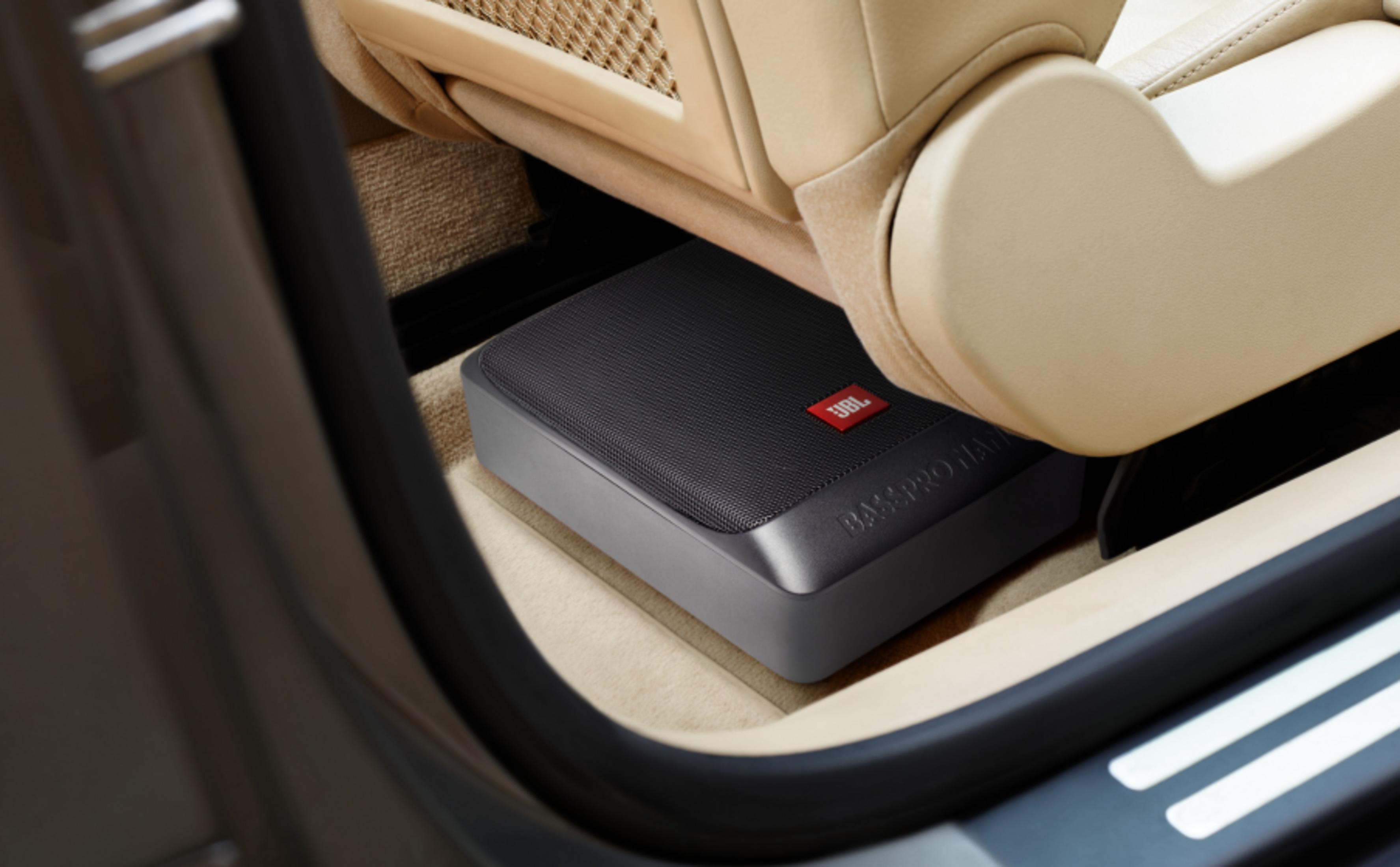Un subwoofer JBL noir est placé sous un siège de voiture beige.