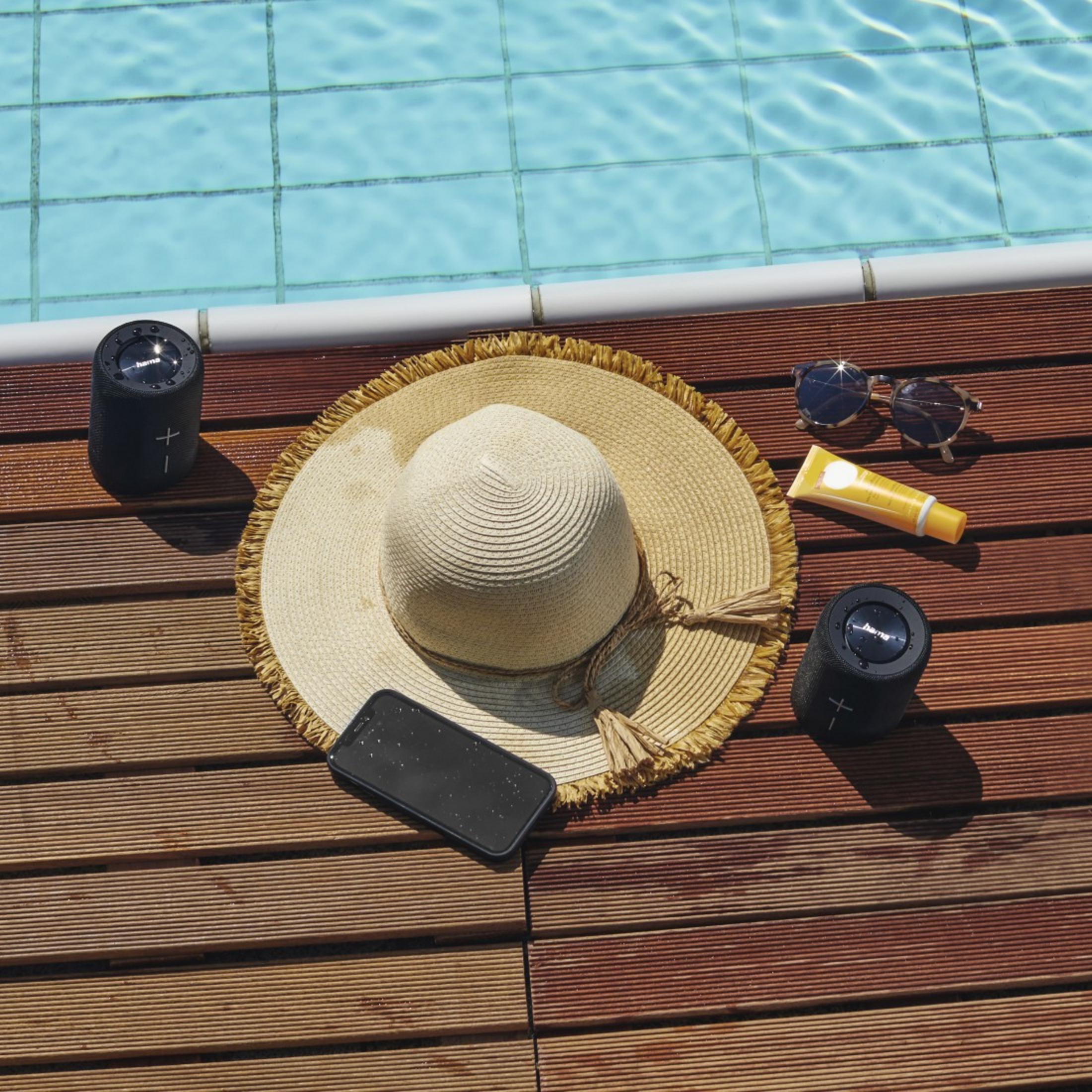 Krem przeciwsłoneczny, kapelusz, głośniki i telefon na drewnianym tarasie przy basenie.