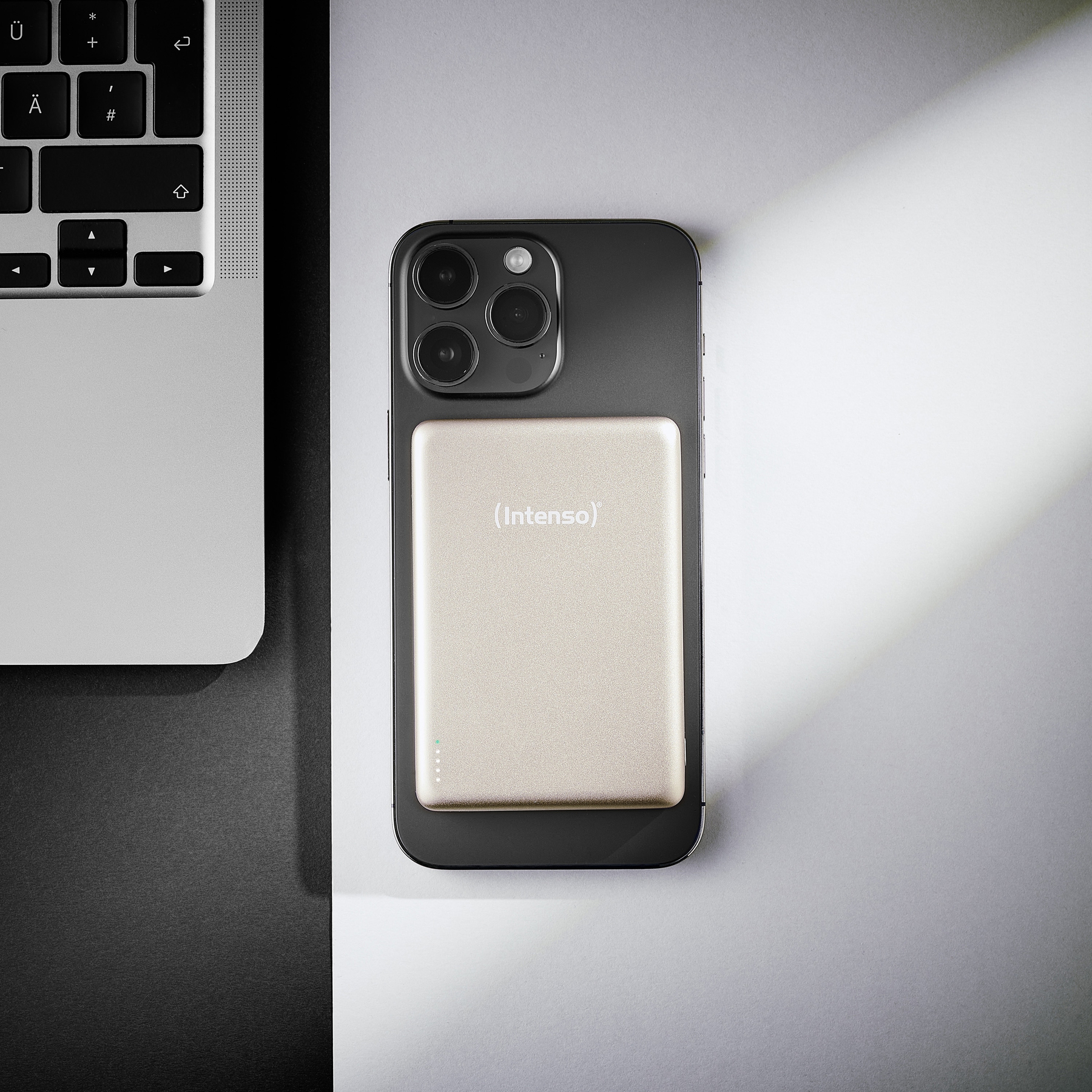 Uno smartphone nero con un power bank dorato e tastiera di un laptop accanto.