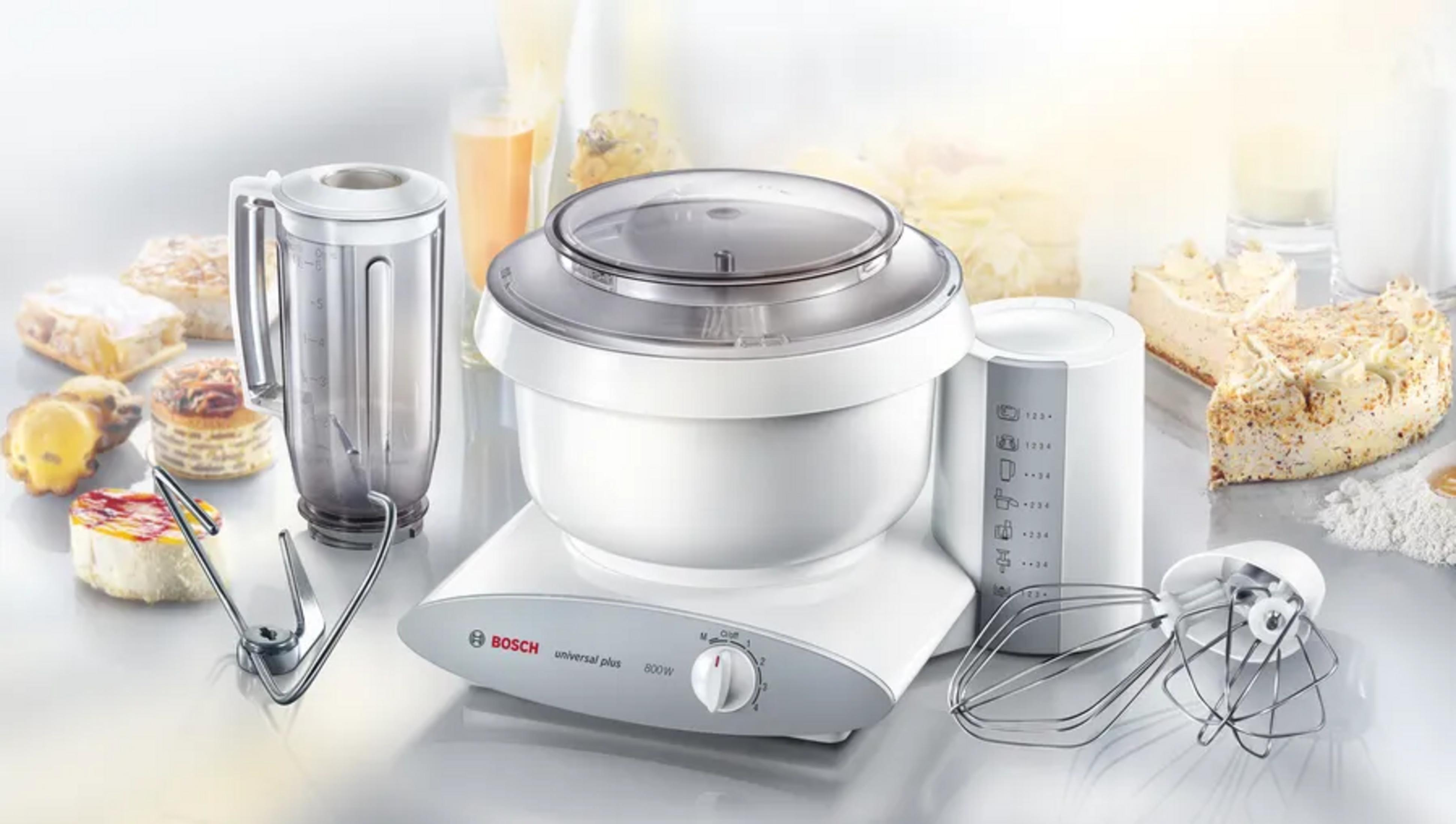 Een witte Bosch keukenmixer met accessoires en stukken taart.