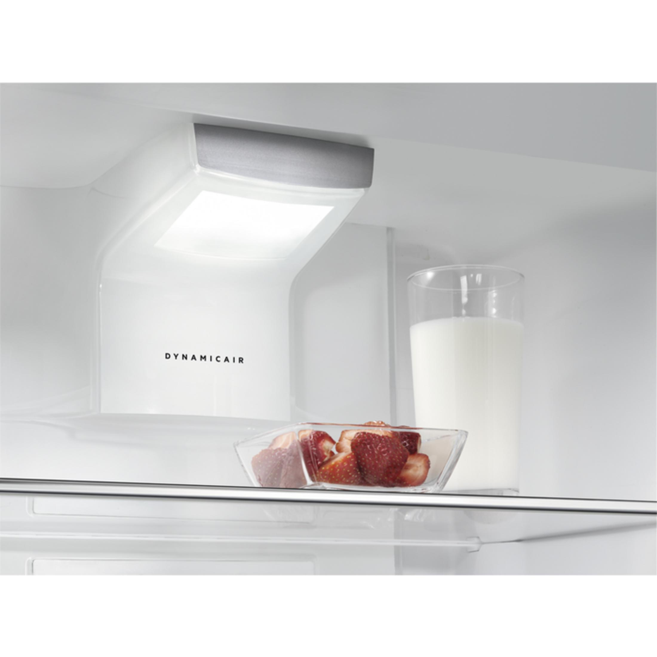 Un vaso de leche y un tazón de fresas en un estante de refrigerador.