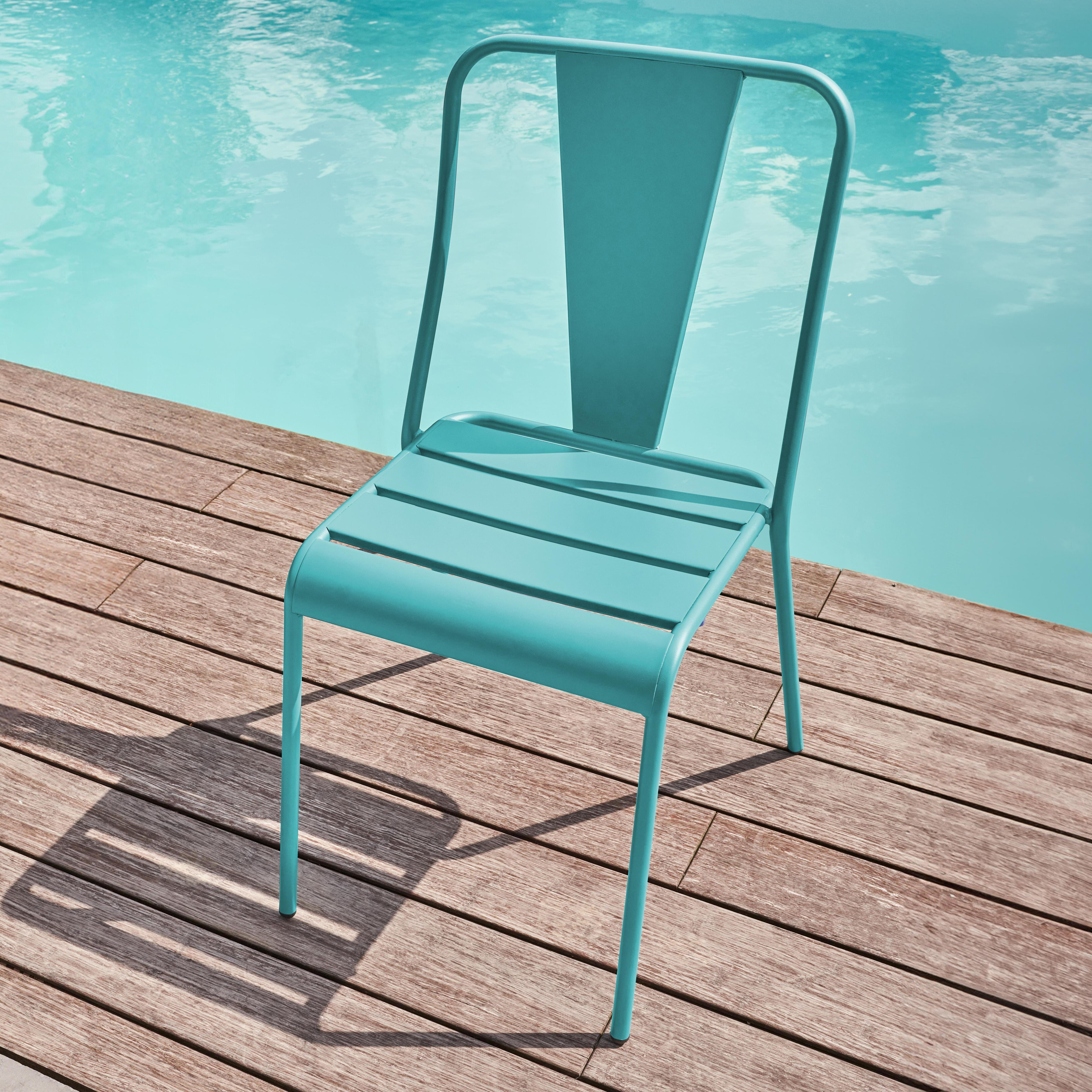 Eine türkisfarbene Metallstuhl steht auf einer Holzterrasse neben einem Pool.