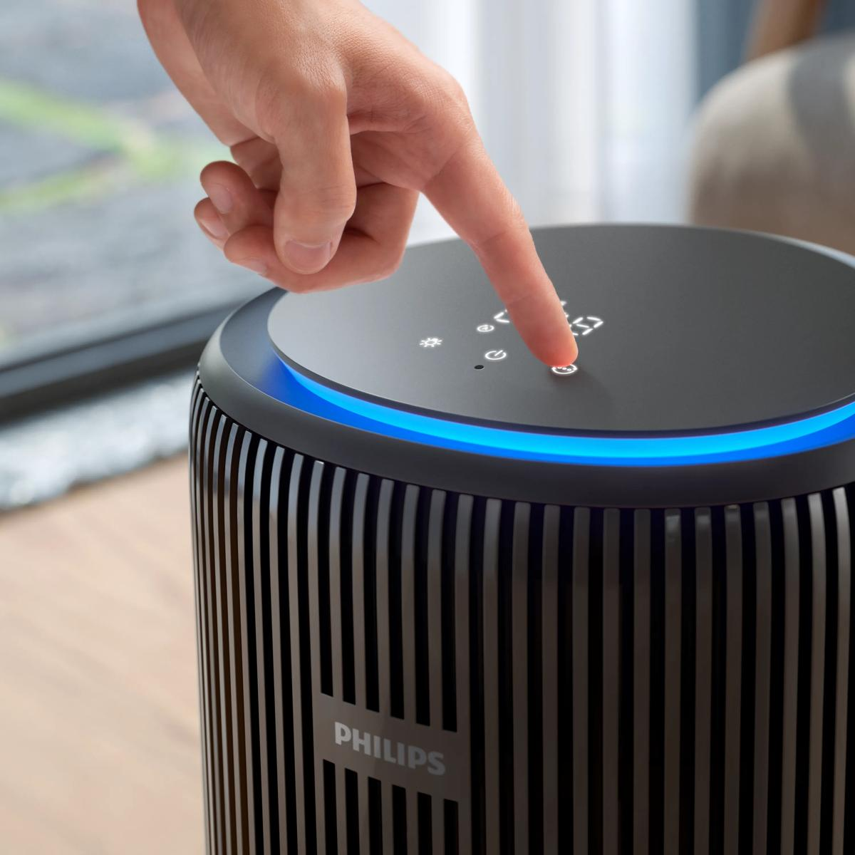 Dłoń naciska przycisk na czarnym oczyszczaczu powietrza Philips z niebieskim podświetleniem.