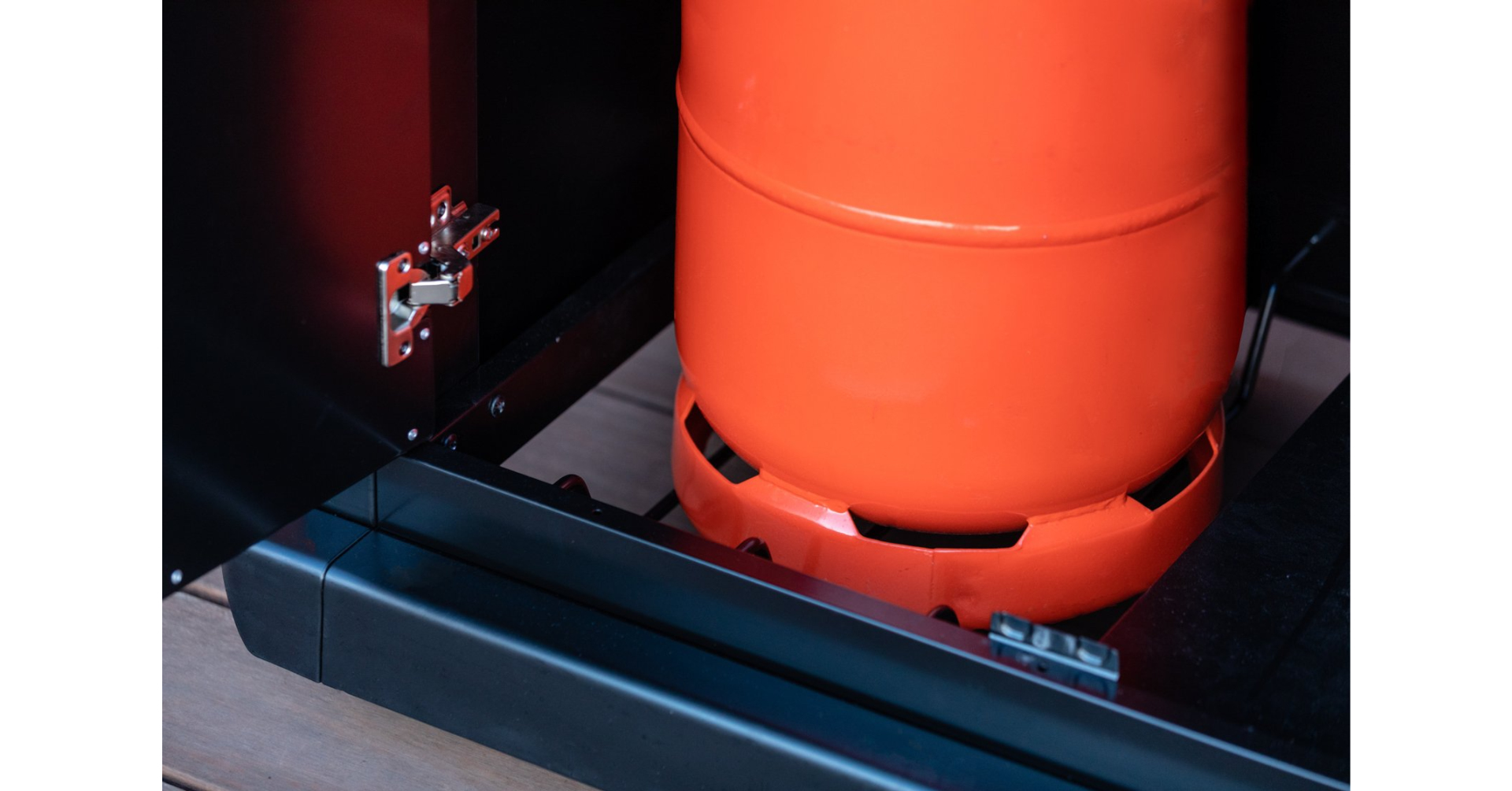 Una bombola del gas arancione si trova all'interno di un armadio nero su pavimento in legno.