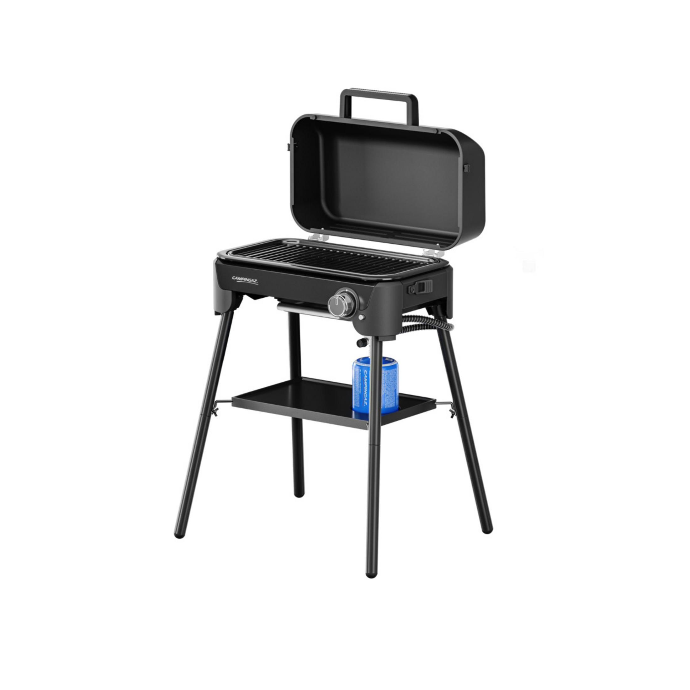 Una griglia portatile nera con coperchio aperto si erge su gambe alte. Una bombola di gas blu è sullo scaffale.