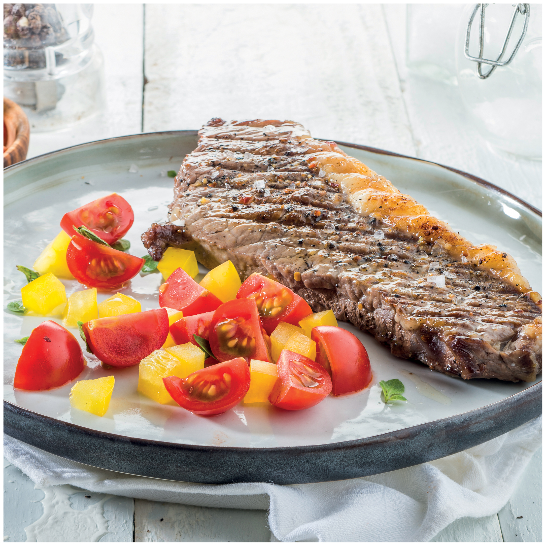Grilled steak with tomato and bell pepper salad on a plate.