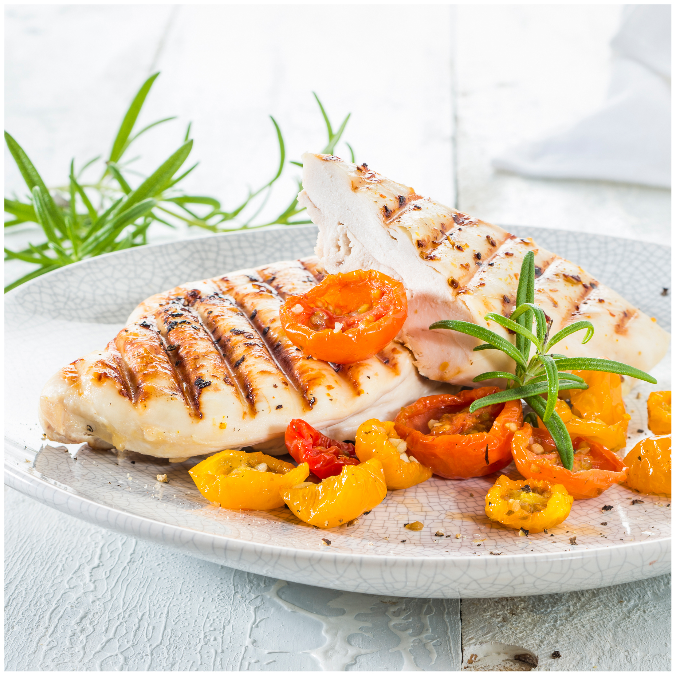 Grilled chicken breast with roasted cherry tomatoes and rosemary on a plate.