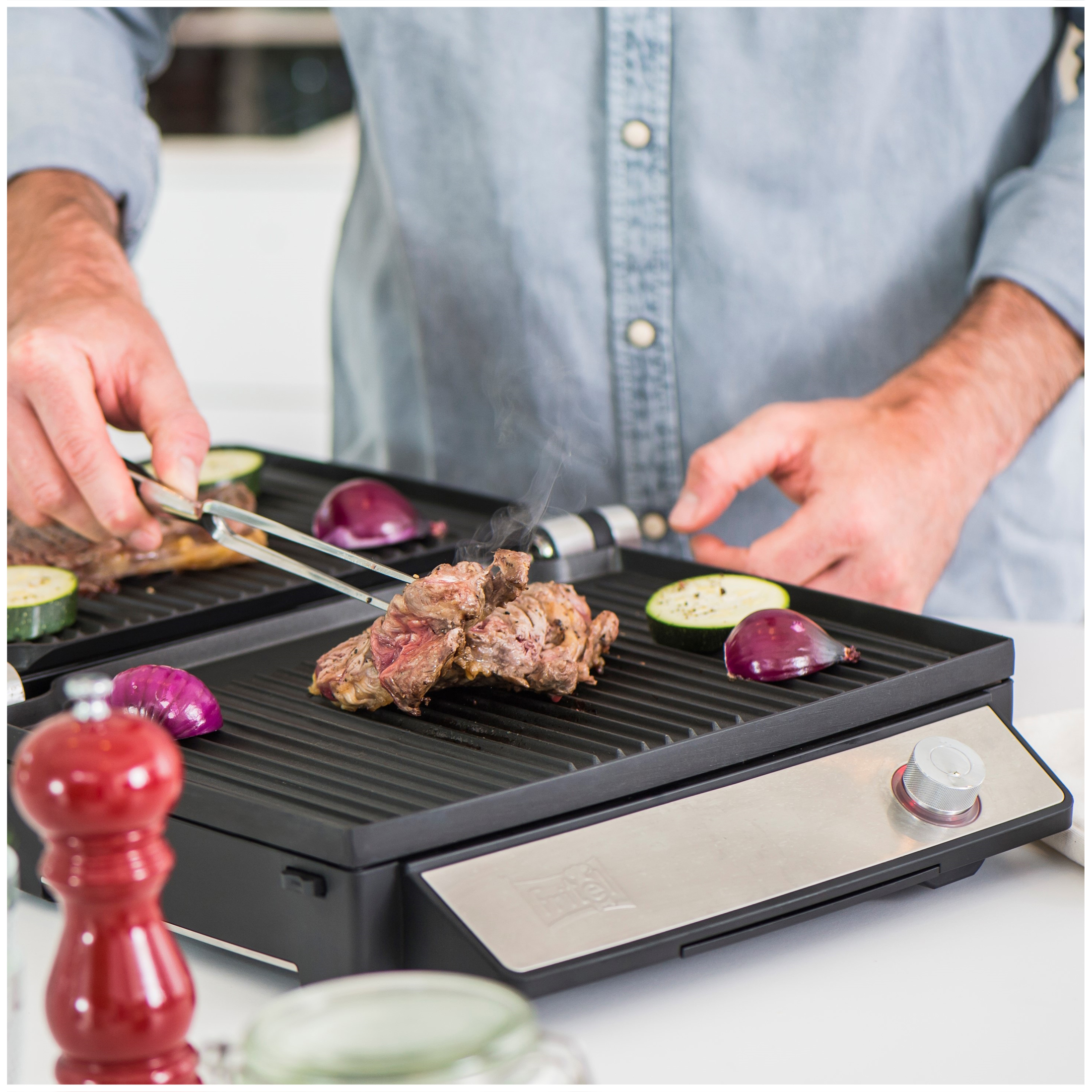 A man grills meat and vegetables on an electric grill.