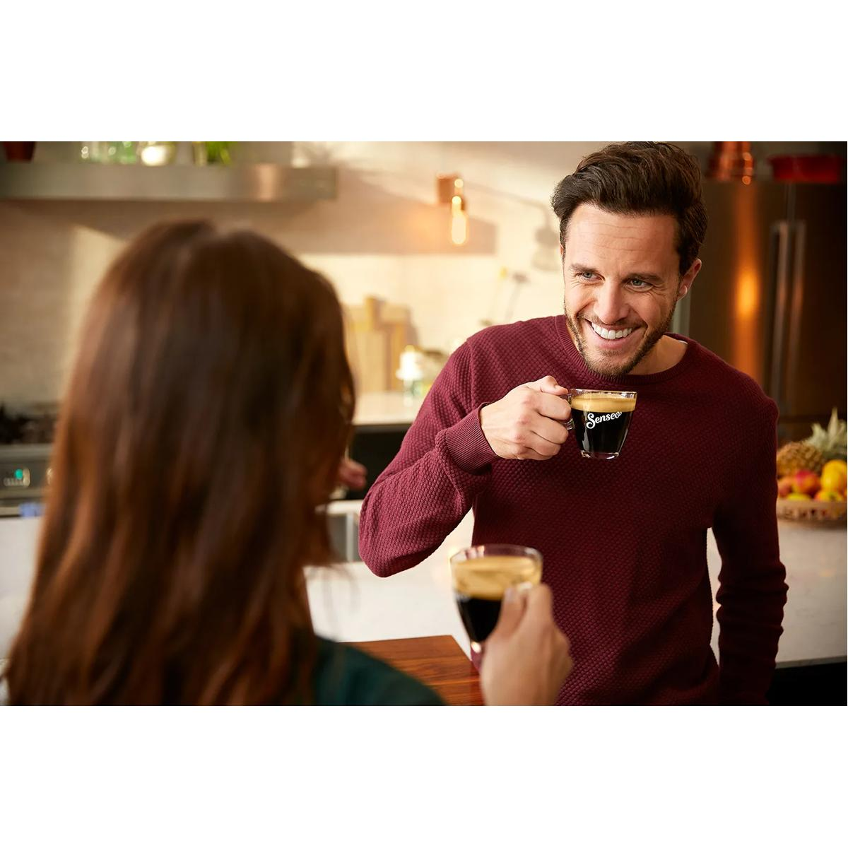 Uomo in maglione bordeaux tiene caffè, sorride alla donna.