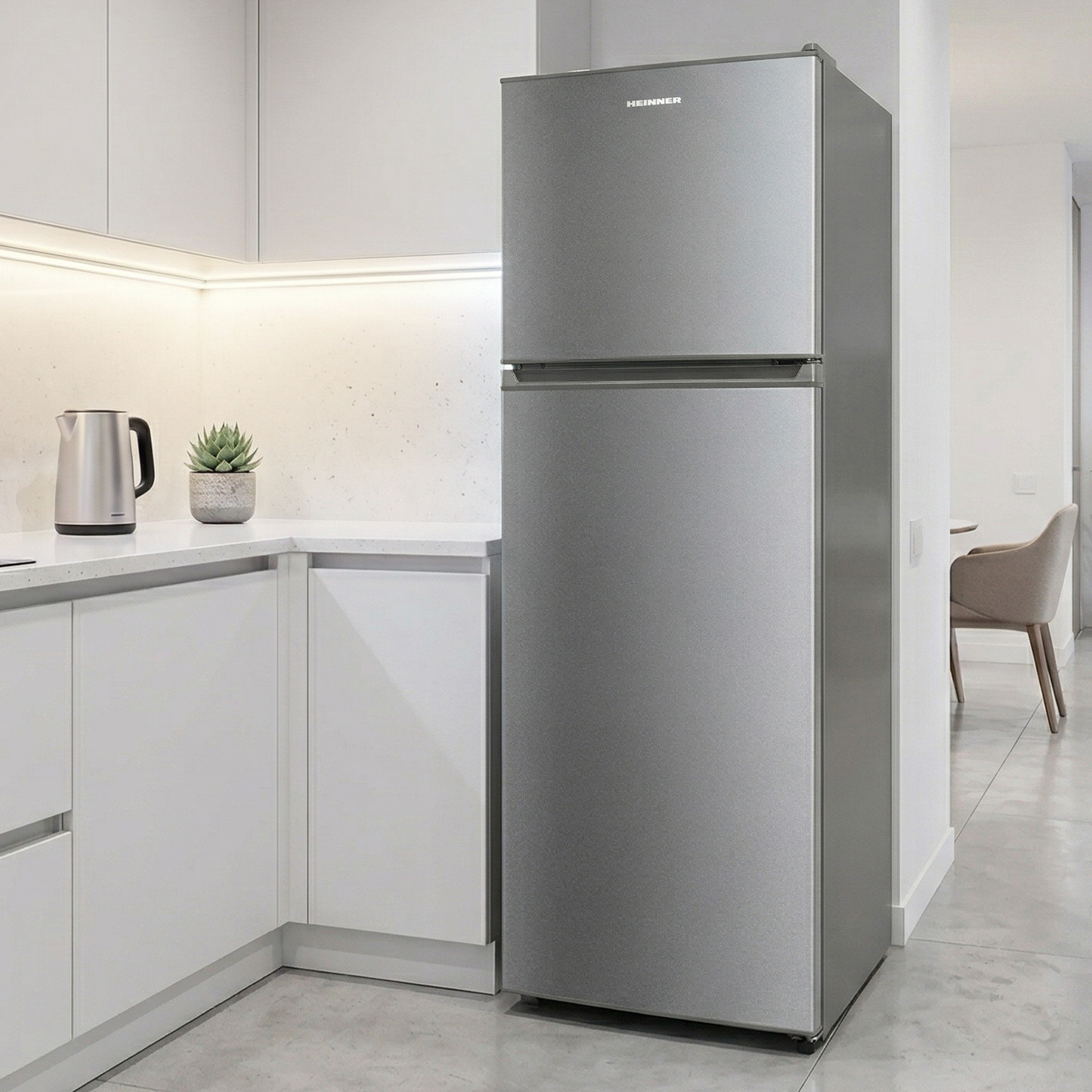 A silver refrigerator stands in a modern kitchen next to white cabinets. A kettle and plant are on the counter.