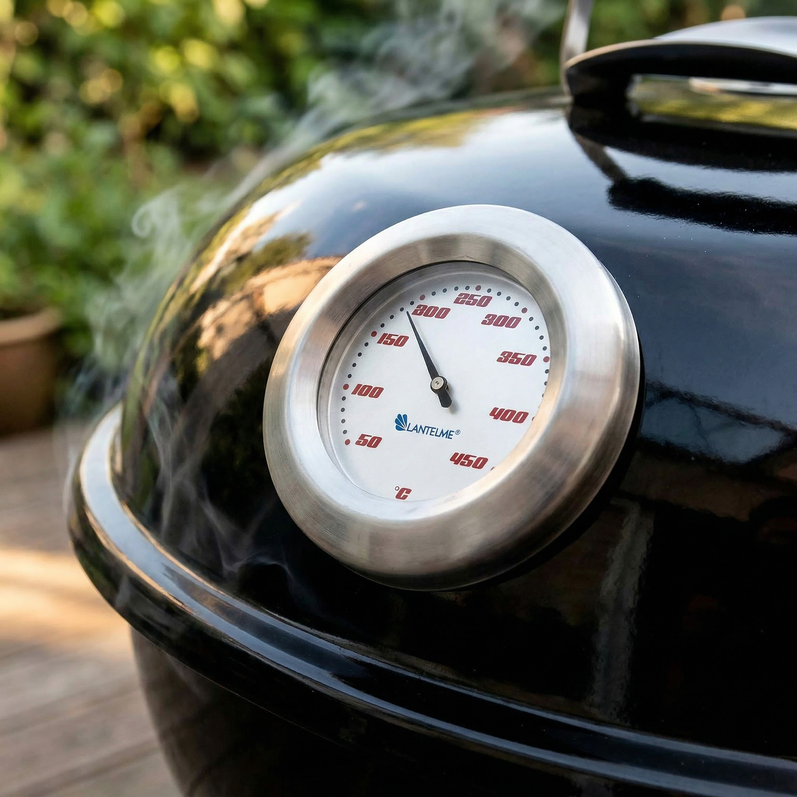 Ein schwarzer Grill mit einem Thermometer, das 150°C anzeigt. Rauch steigt auf.