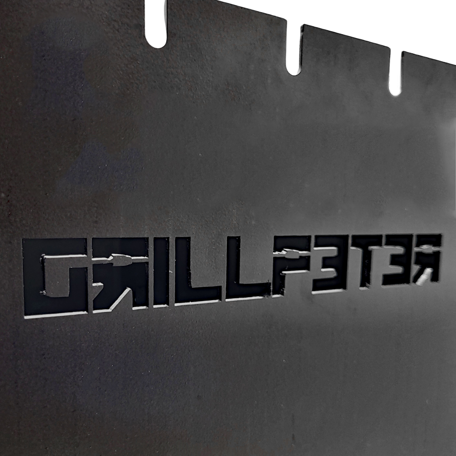 Schwarzes Metallschild mit ausgeschnittenen Buchstaben GRILLMASTER. Oberkante hat Kerben.
