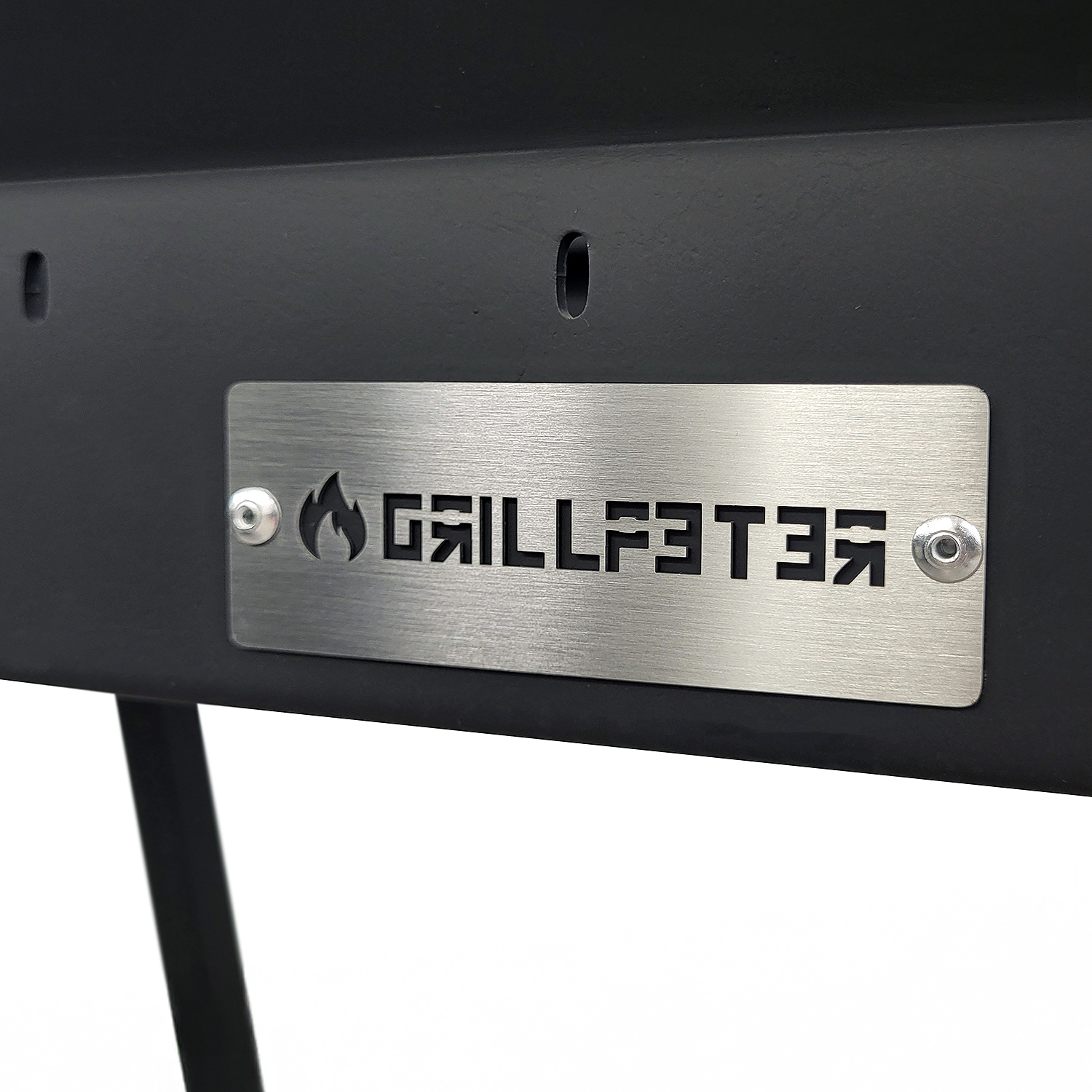 Metallschild mit Flammenlogo und Schriftzug GRILLFEUER, an einem schwarzen Gerät befestigt.
