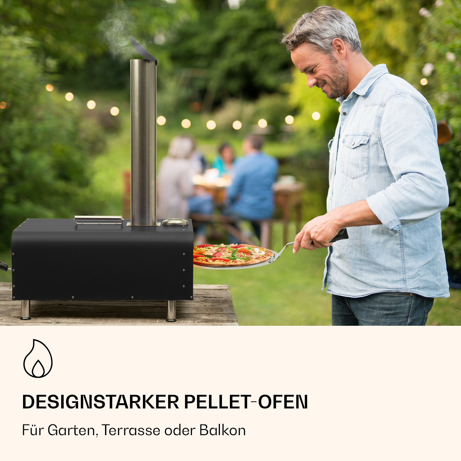 Mann im blauen Hemd präsentiert Pizza aus schwarzem Pelletofen im Garten.