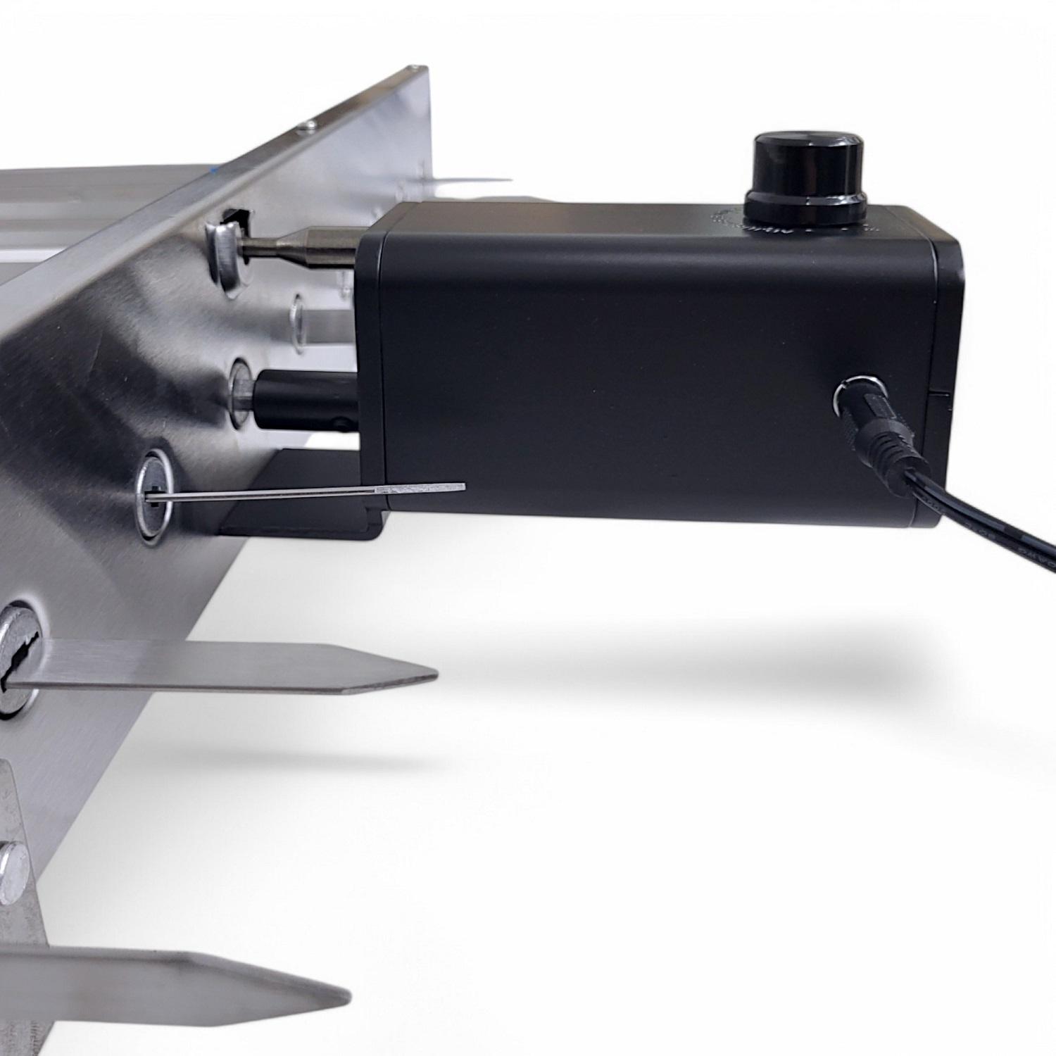 Ein schwarzer Motor mit Drehknopf ist an einem Edelstahlgehäuse befestigt. Es gibt Spieße.