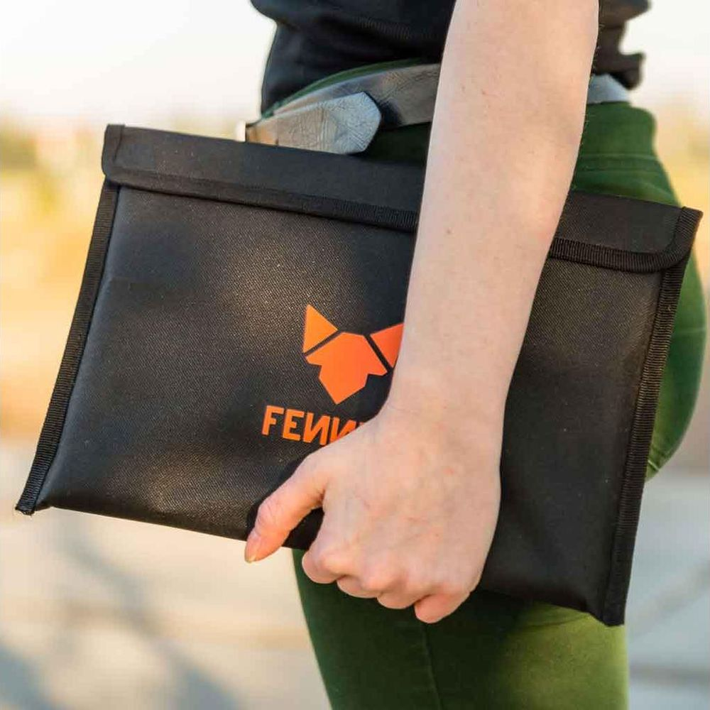 Eine Person hält eine schwarze Tasche mit orangefarbenem Logo und Schriftzug.