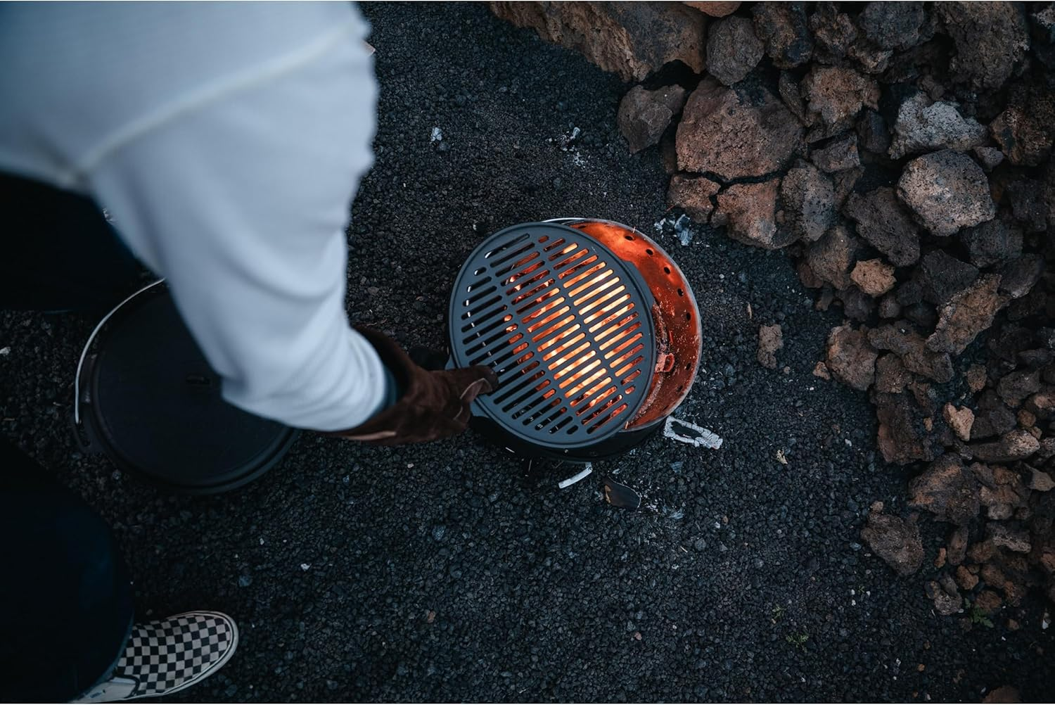 Person mit Handschuh setzt Grillrost auf glühende Kohlen.