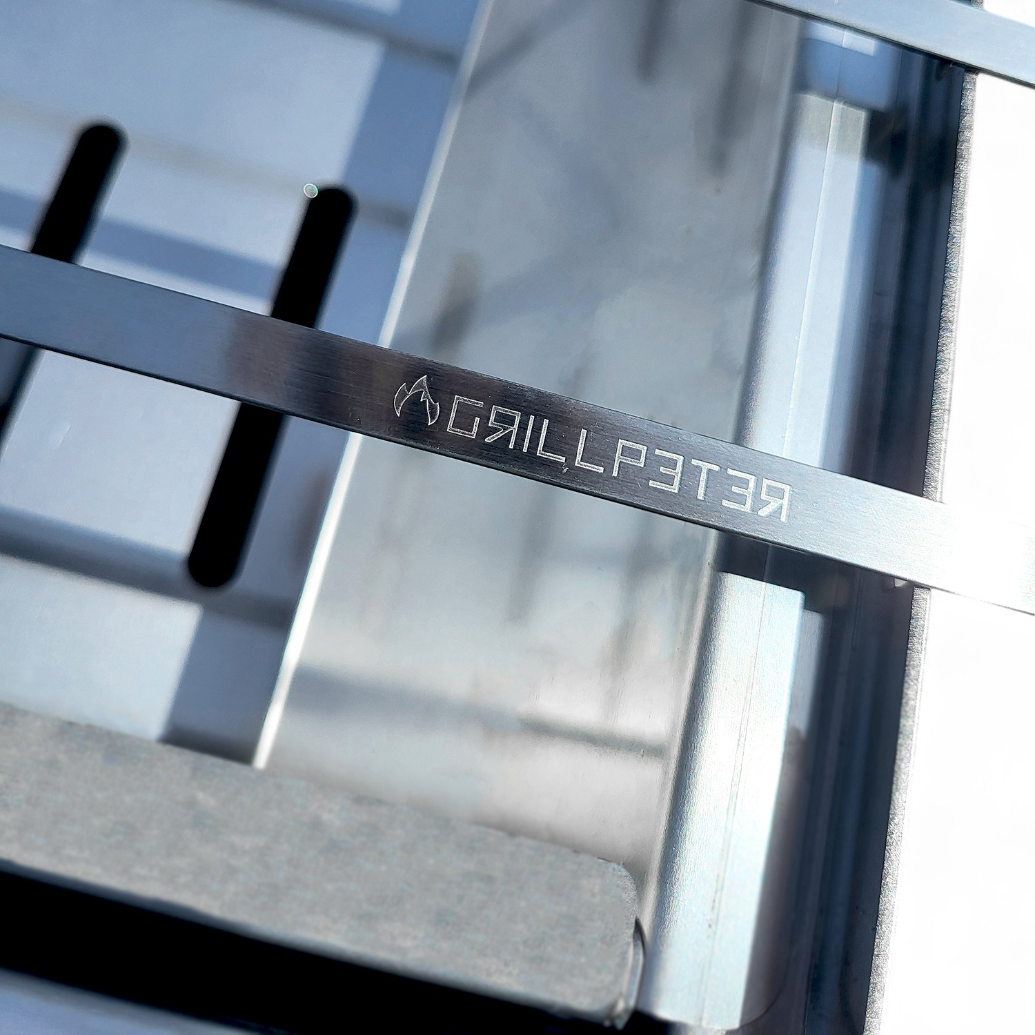 Nahaufnahme eines silbernen Grillrostes mit dem eingeätzten Logo "GRILLPETER".