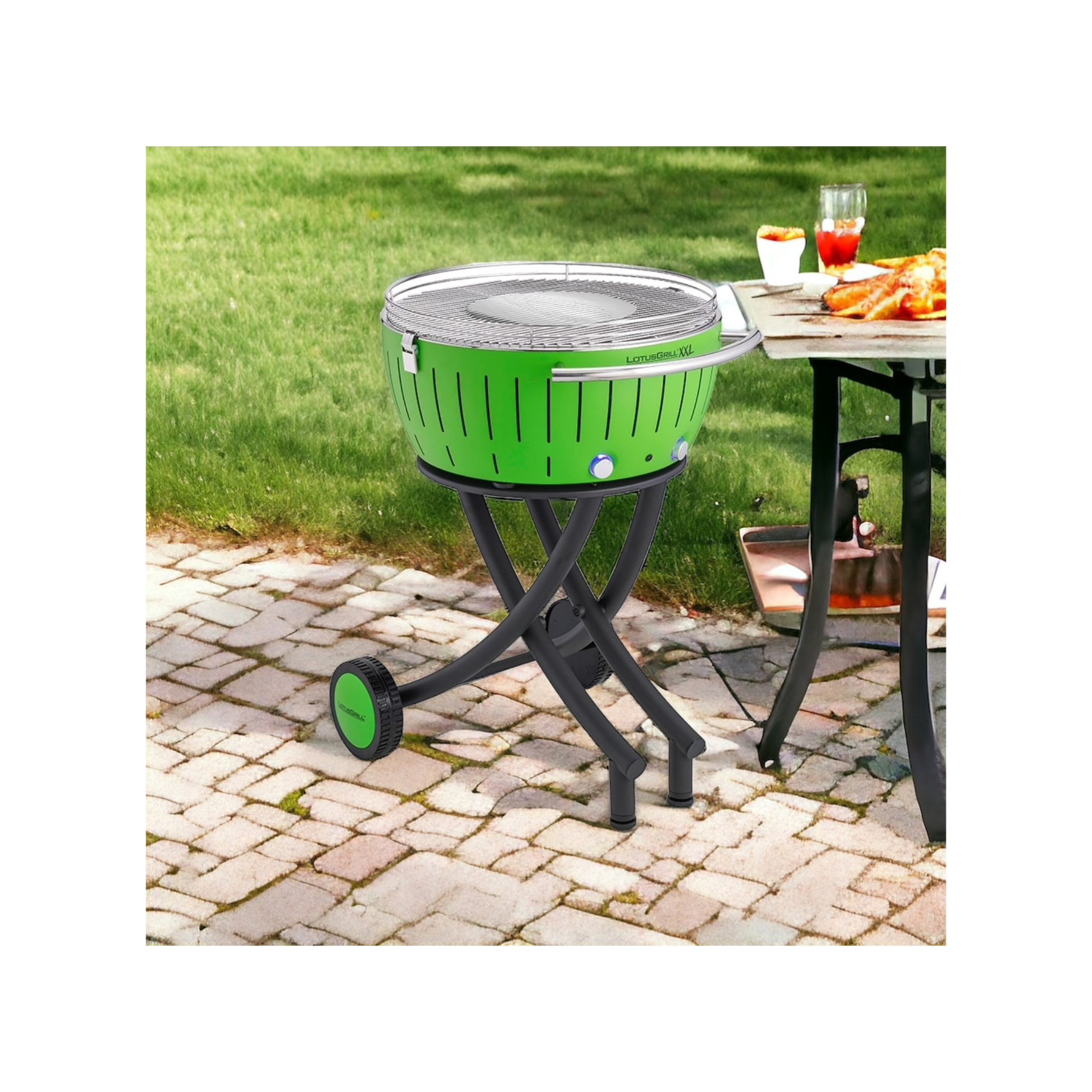 Ein grüner LotusGrill XXL auf einem Untergestell mit Rädern, daneben ein Tisch mit Essen.