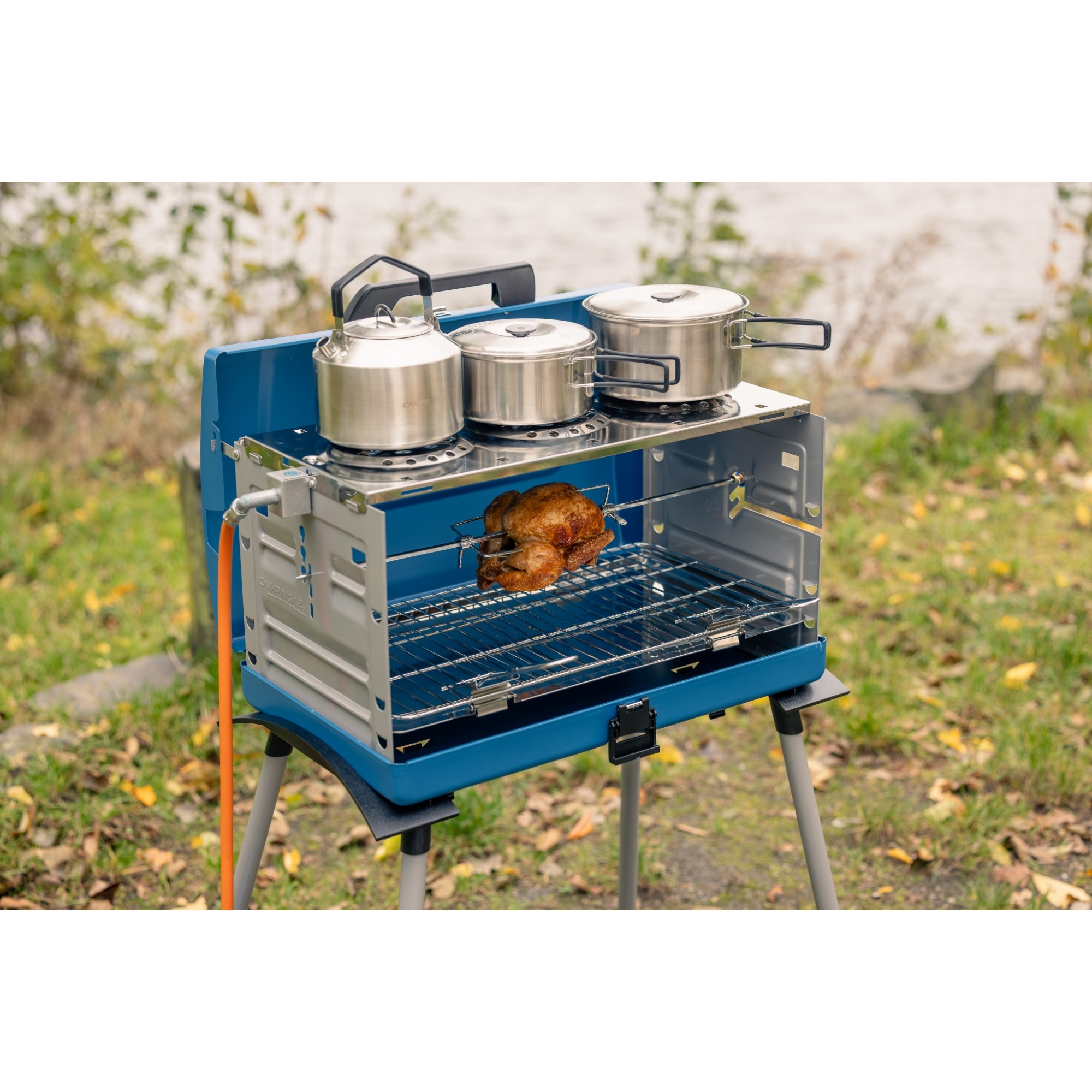 Un fornello da campeggio blu con pollo arrosto all'interno, bollitore e pentole sopra.