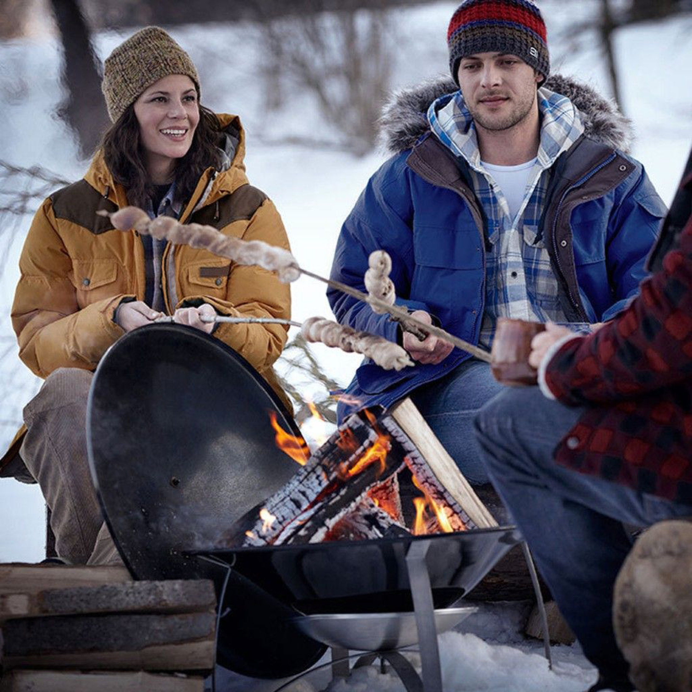 Personas con ropa de invierno asan comida sobre una fogata en la nieve.