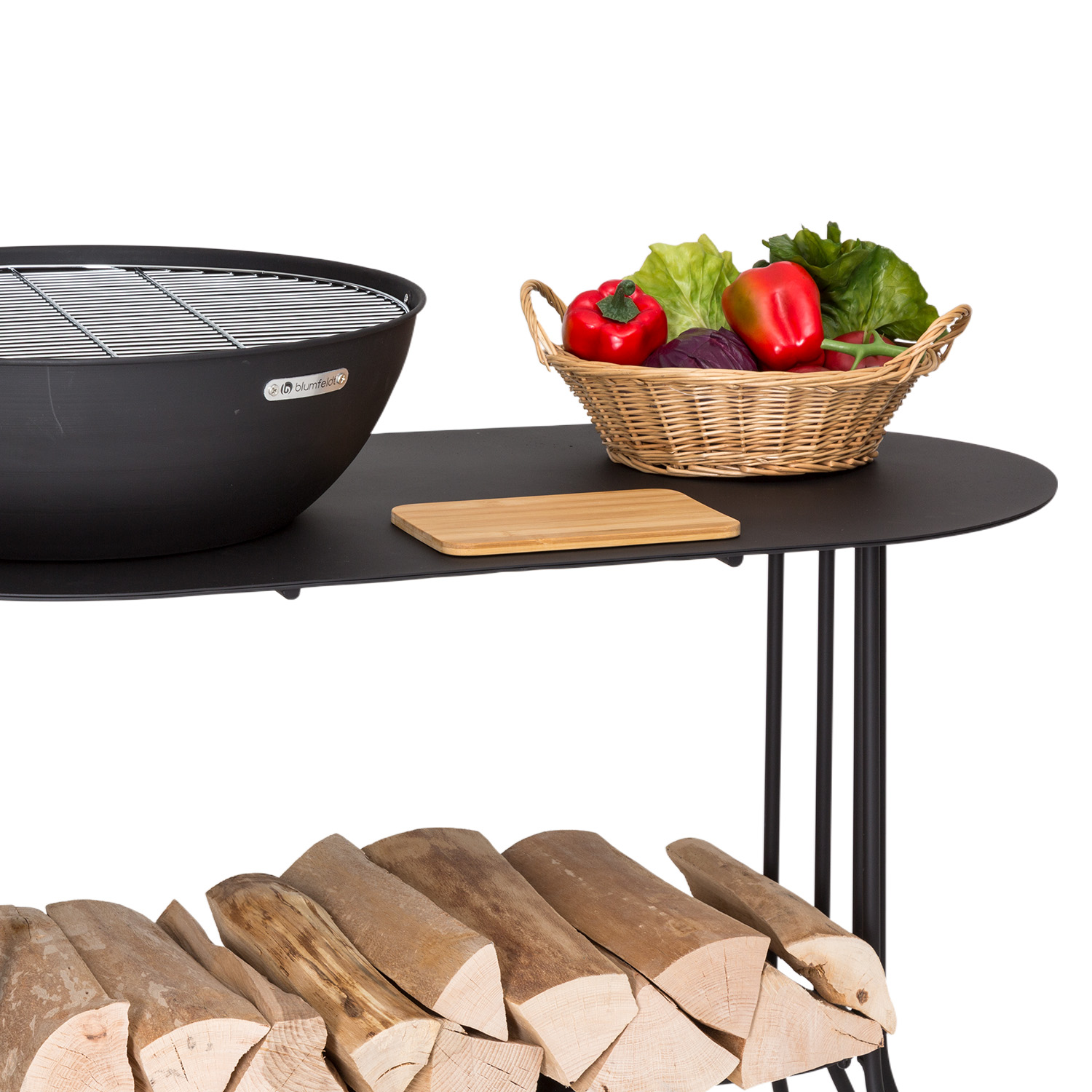 Ein schwarzer Grill steht auf einem Tisch neben einem Korb mit Gemüse und Holzscheiten.