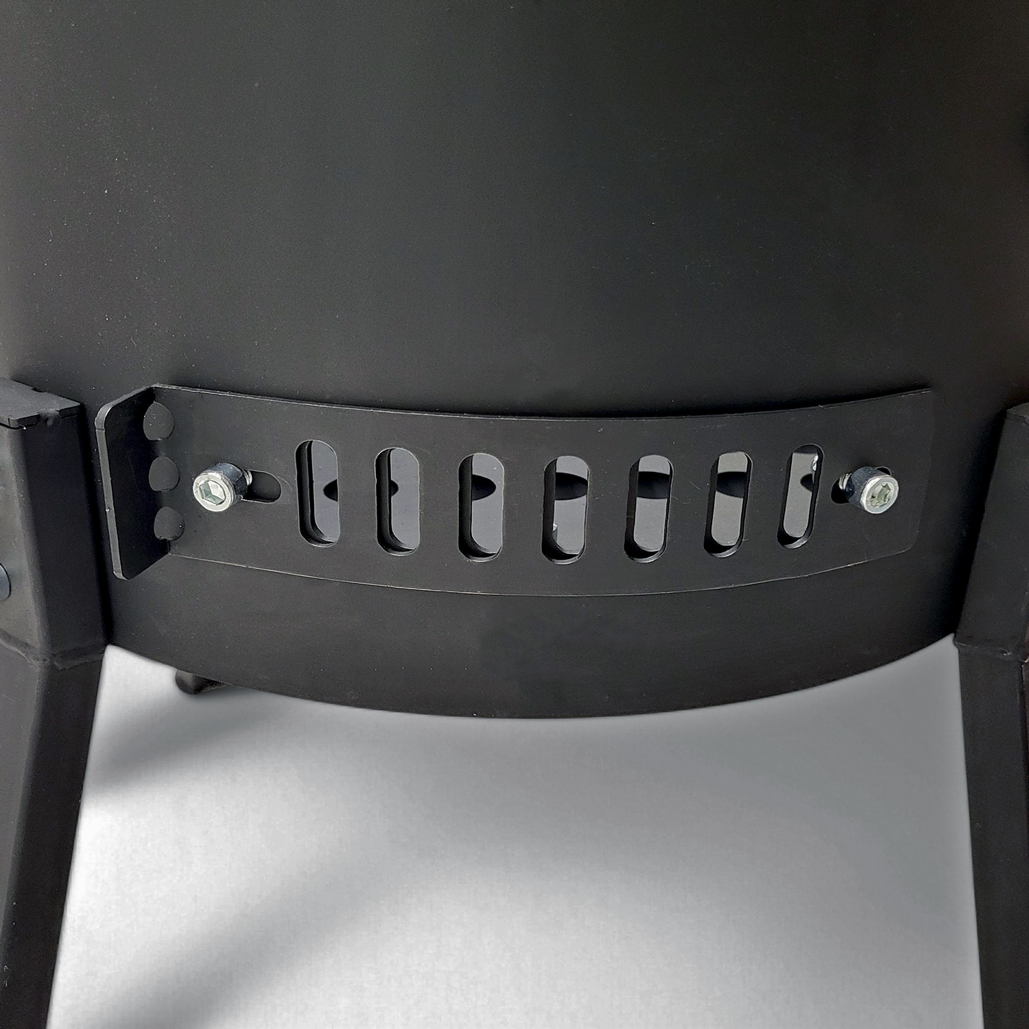 Nahaufnahme eines schwarzen Grills mit Lüftungsschlitzen und Schrauben.