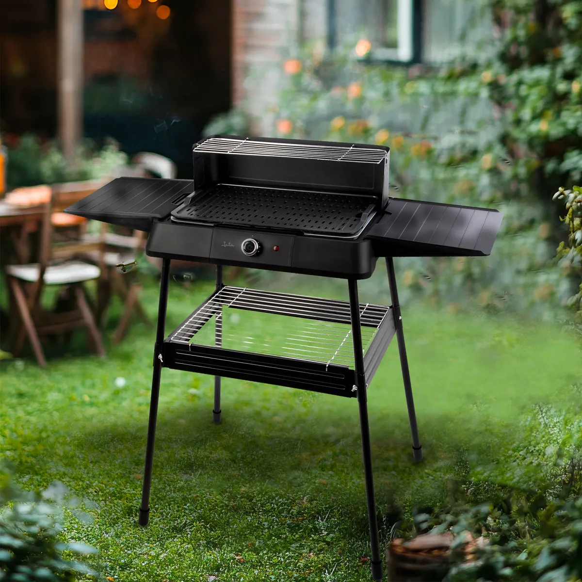 Una parrilla eléctrica negra se alza sobre un césped verde, con mesa y sillas al fondo.