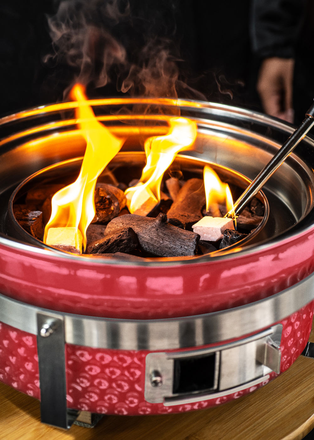 Una parrilla roja con carbón y llamas, atendida con pinzas.