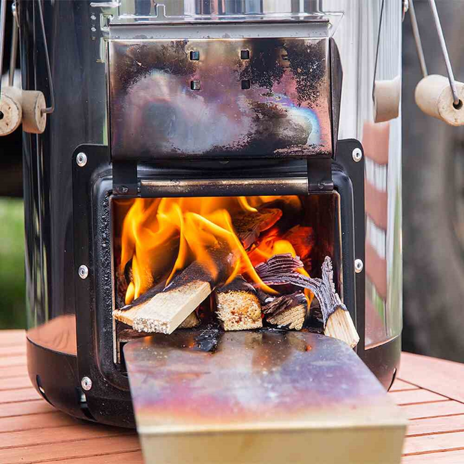 Ein tragbarer Holzofen mit Flammen und Holz im Inneren, auf einem Holztisch.