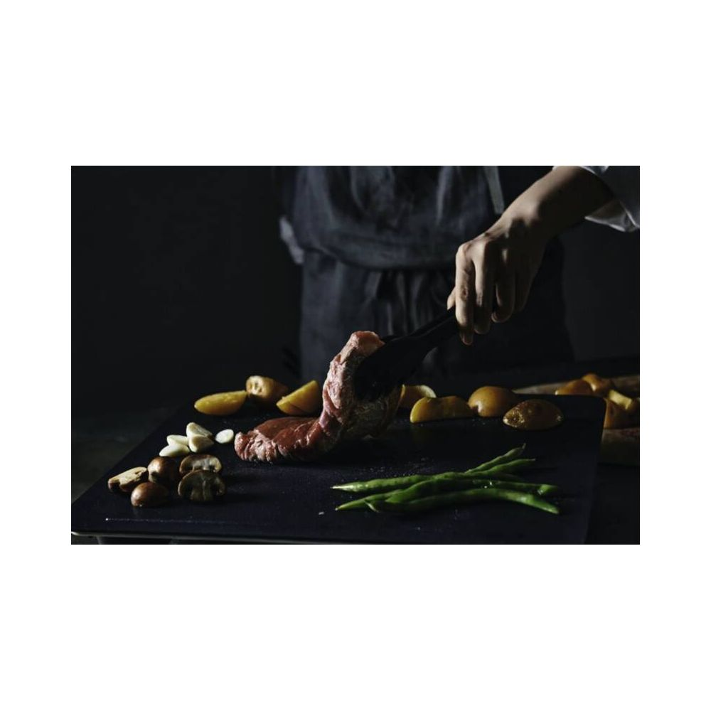 Fleisch mit Zange und Gemüse auf einem schwarzen Brett.