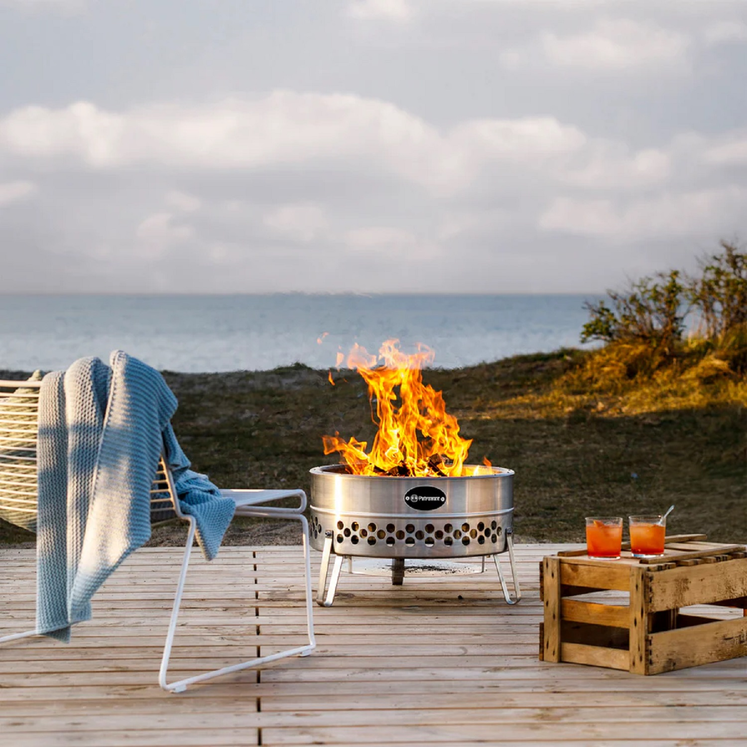 Ein brennendes Feuerbecken am Strand mit zwei Gläsern Cocktail auf Holzkiste.