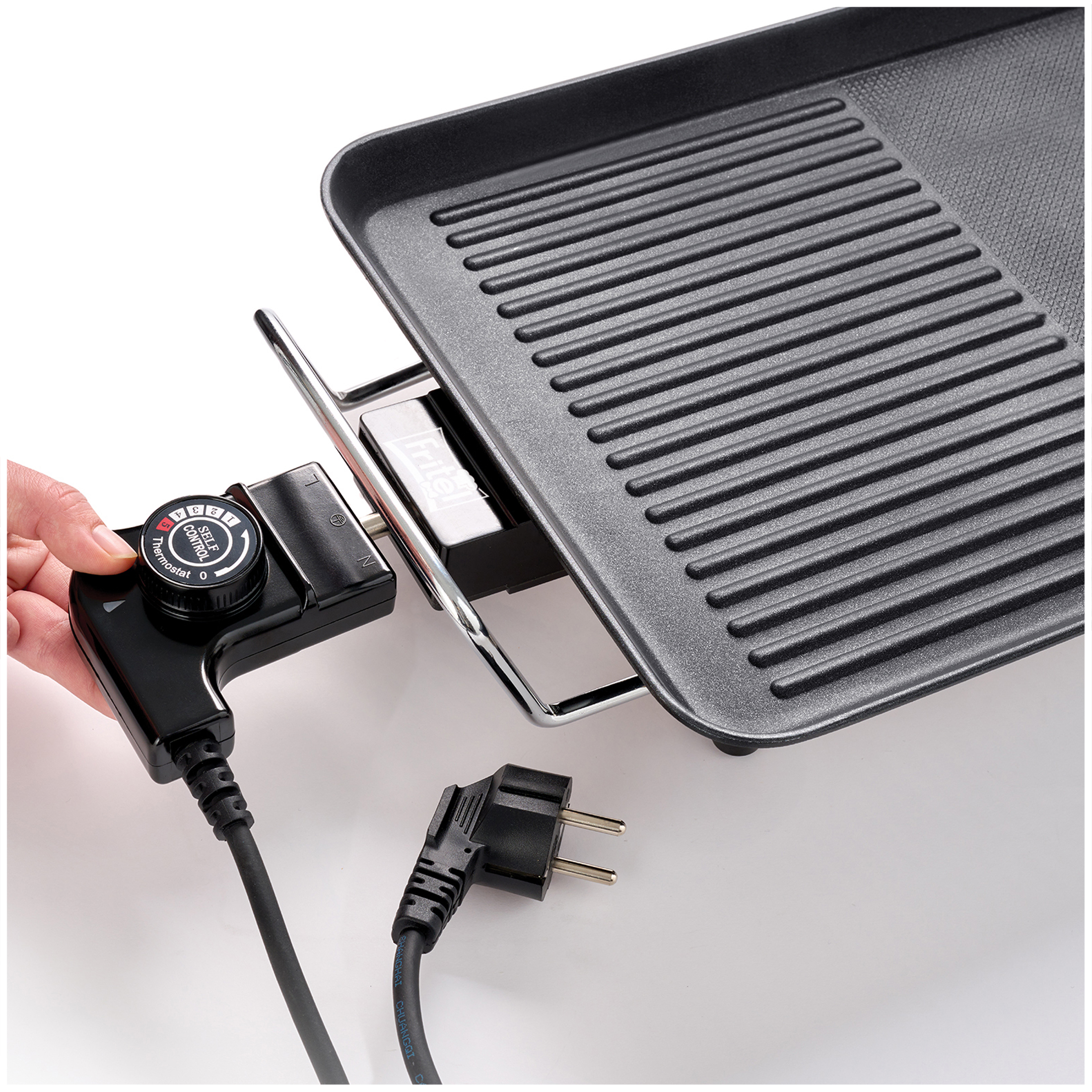 A hand adjusts the thermostat dial on a black electric grill with a cord.