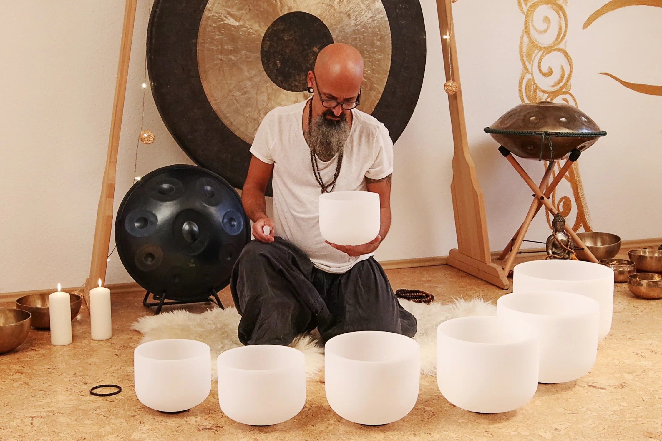 Erkek, gong ve handpan önünde kristal kaselerle diz çöküyor.
