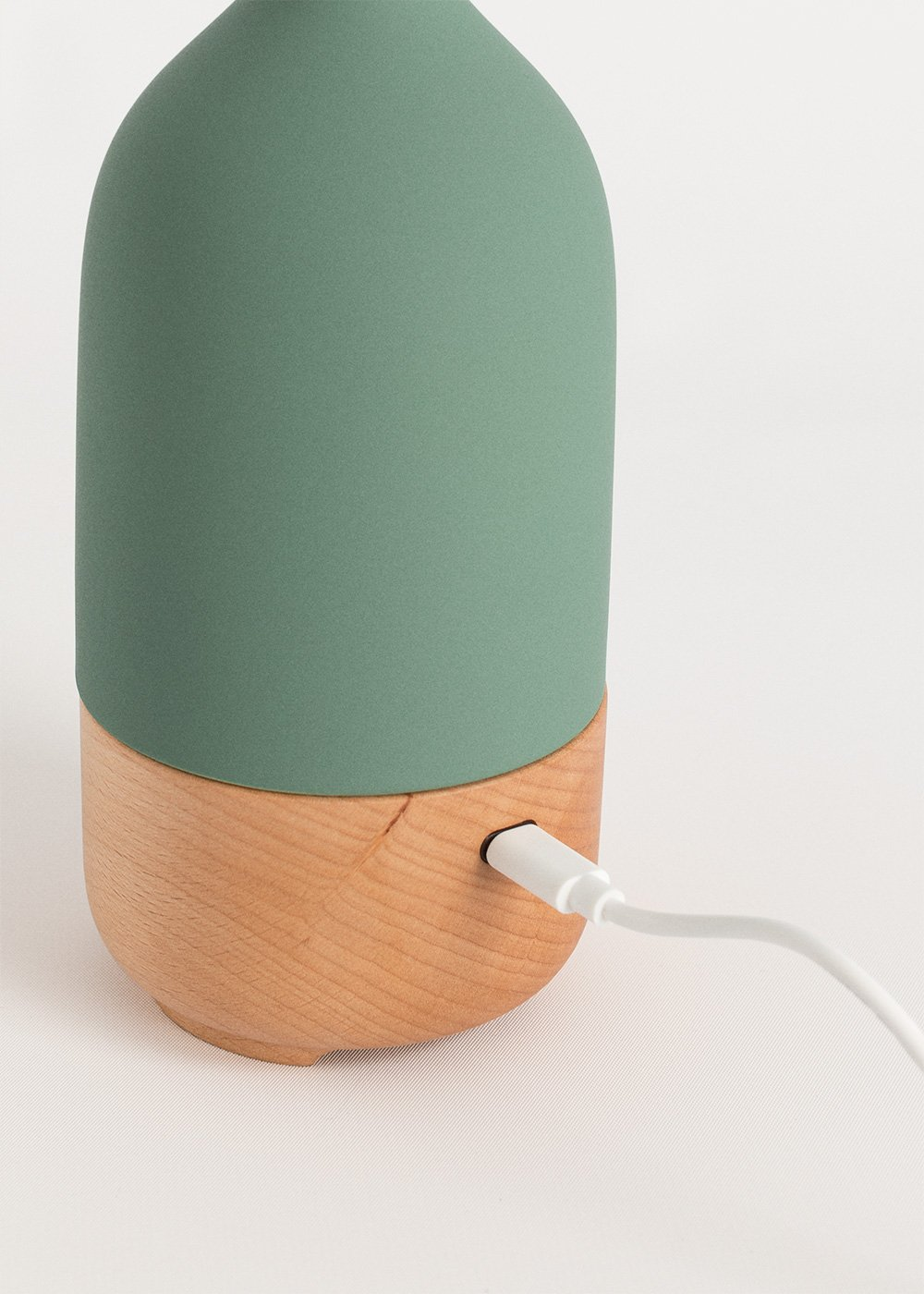 Lámpara verde con base de madera y cable de carga blanco.
