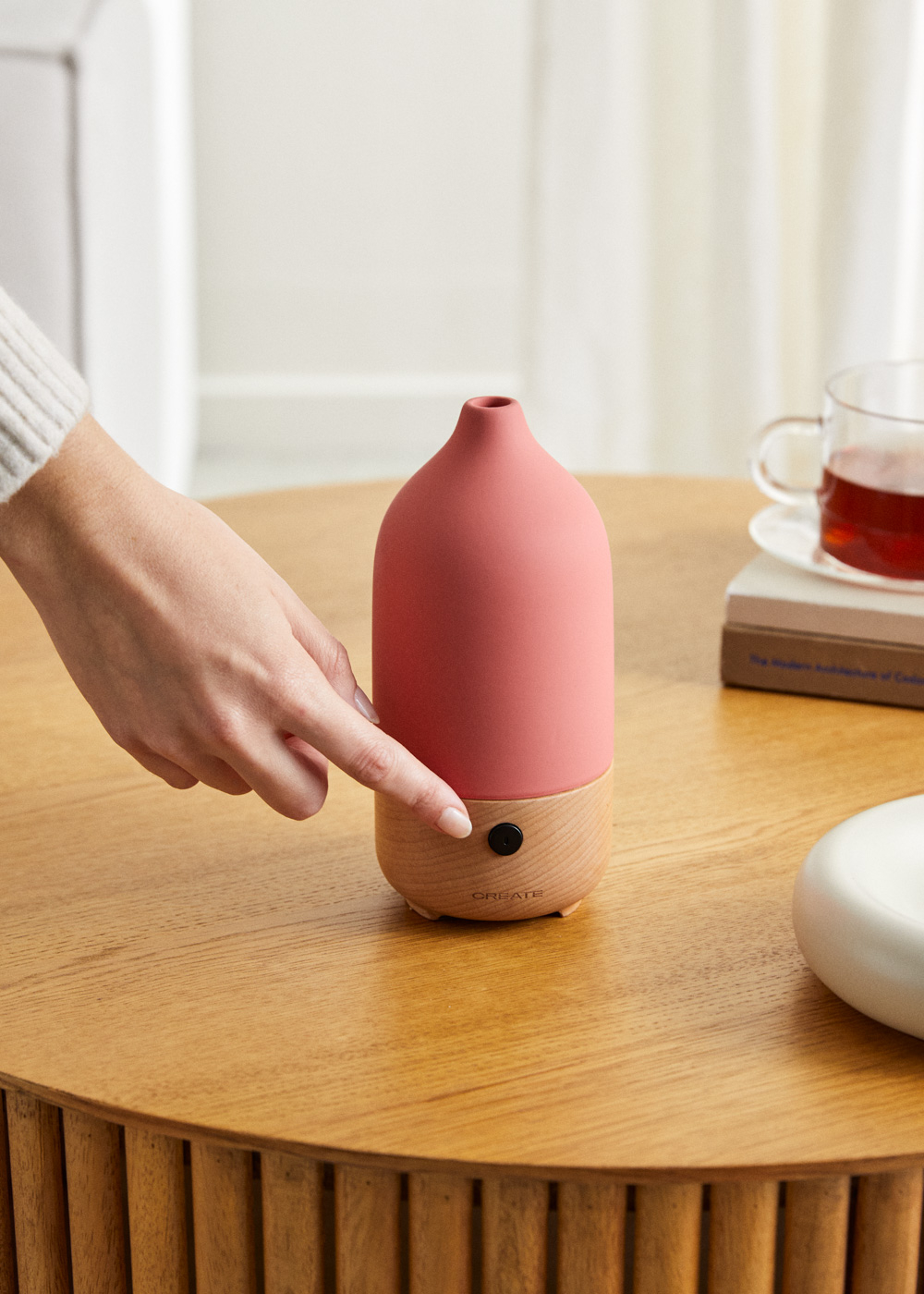 Una mano presiona un botón en un difusor de aceites esenciales rosa y madera.