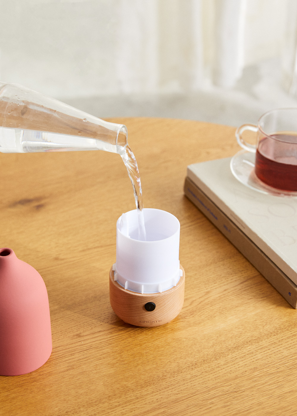 Se vierte agua de una botella transparente en un difusor blanco y de madera sobre una mesa de madera.